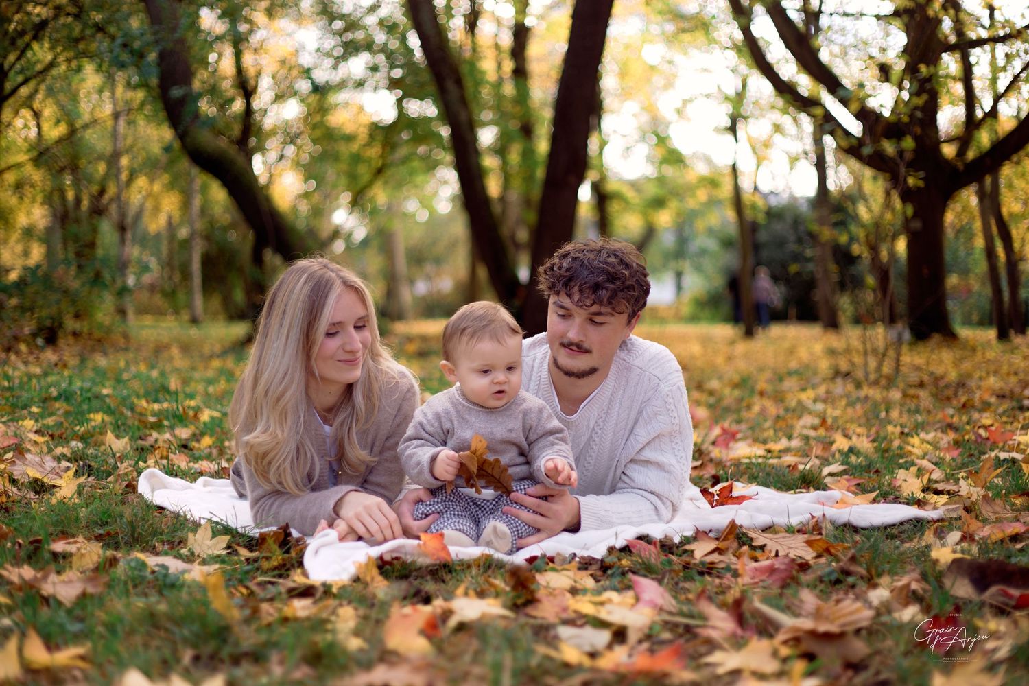 A family relaxes together on a blanket during a fall photo session in a park.