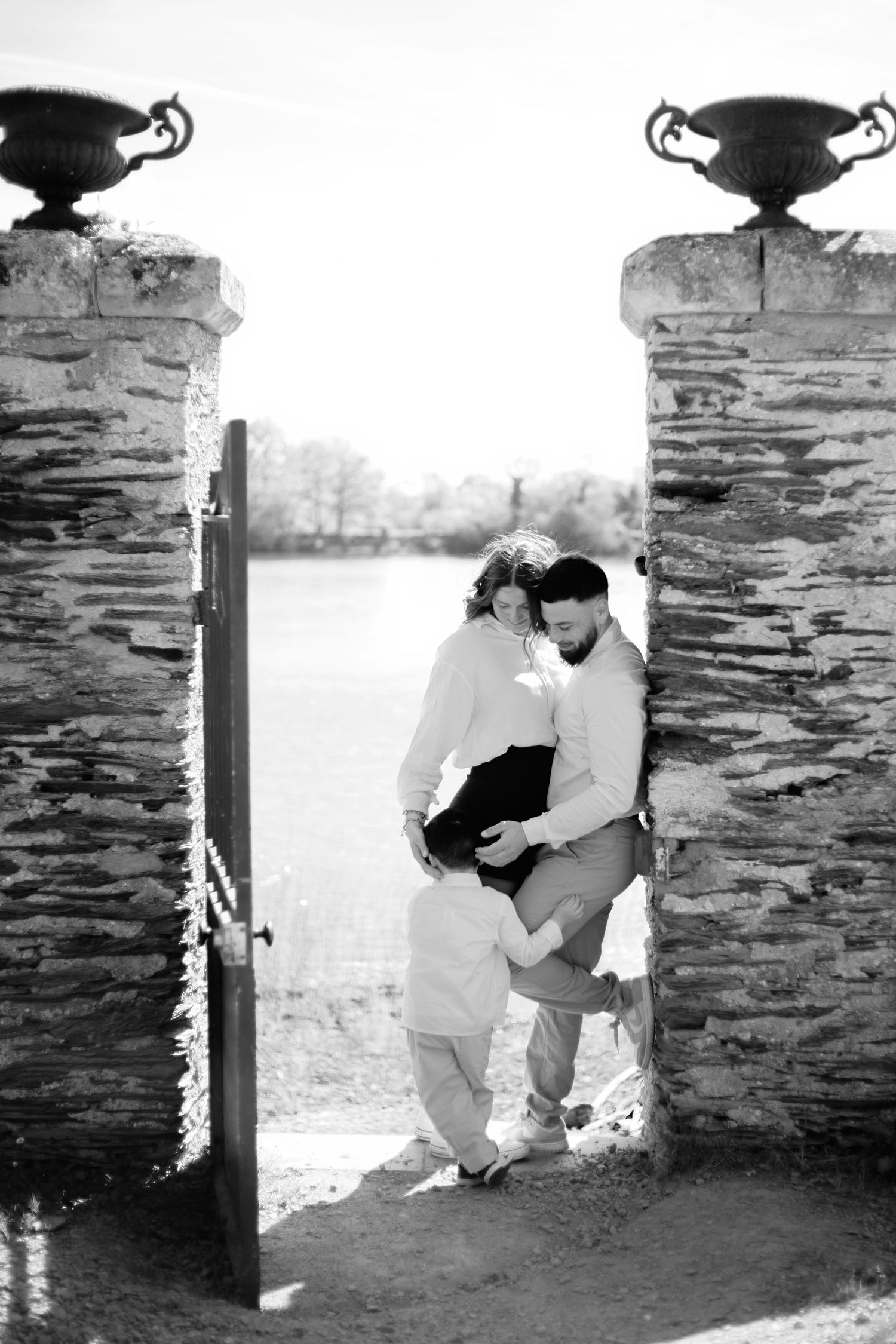 Black and white photo of a family with a young child embracing between stone gate pillars overlooking a scenic landscape.