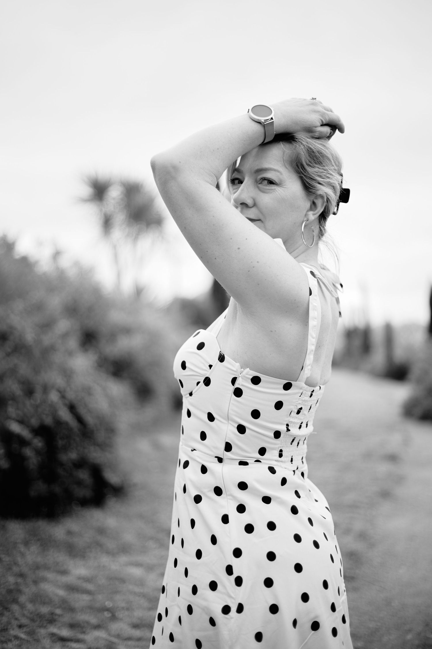 Black and white photo of a woman in a polka dot dress posing outdoors with her arm raised gracefully.