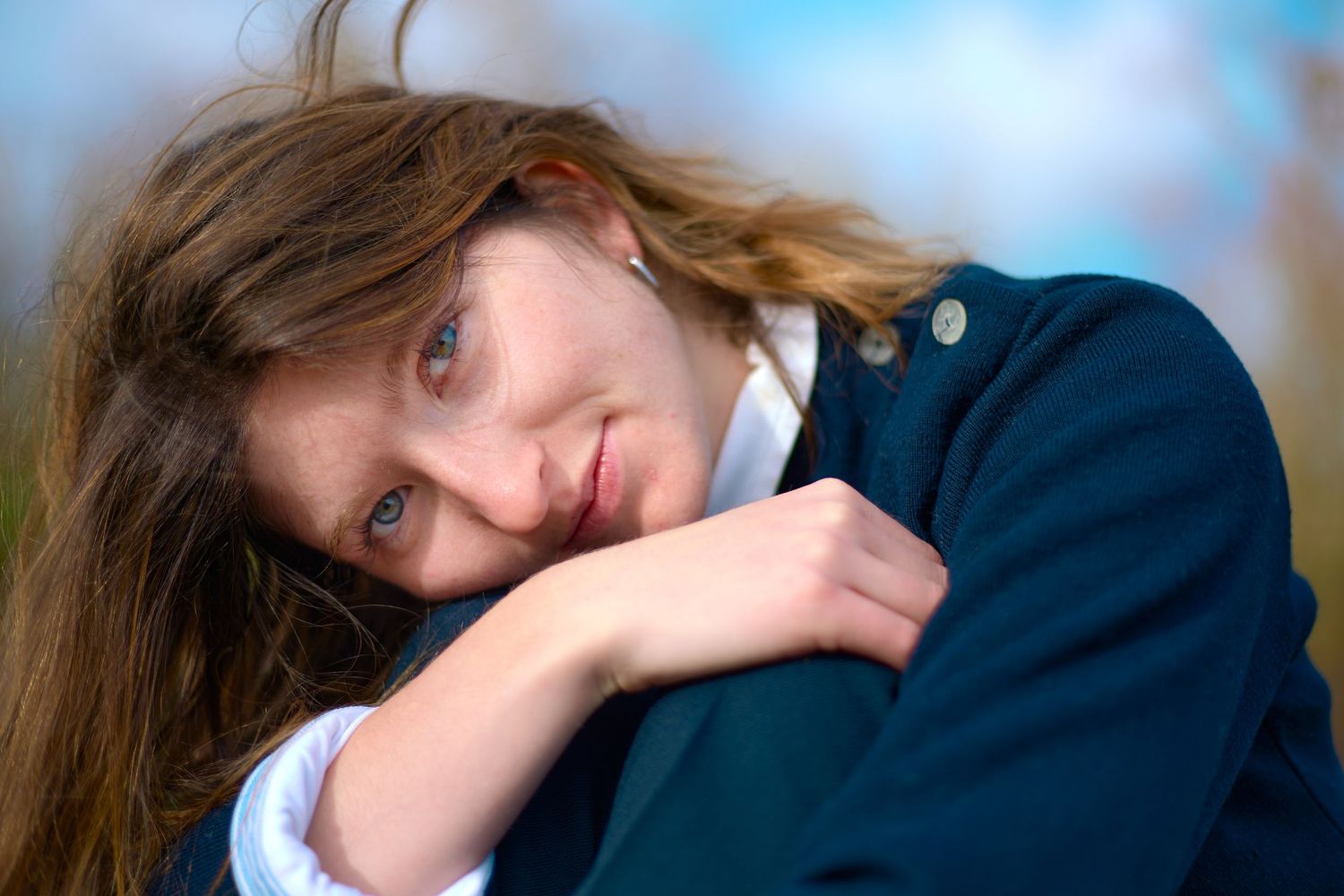 Candid portrait of person in navy jacket resting head on hand with soft lighting.