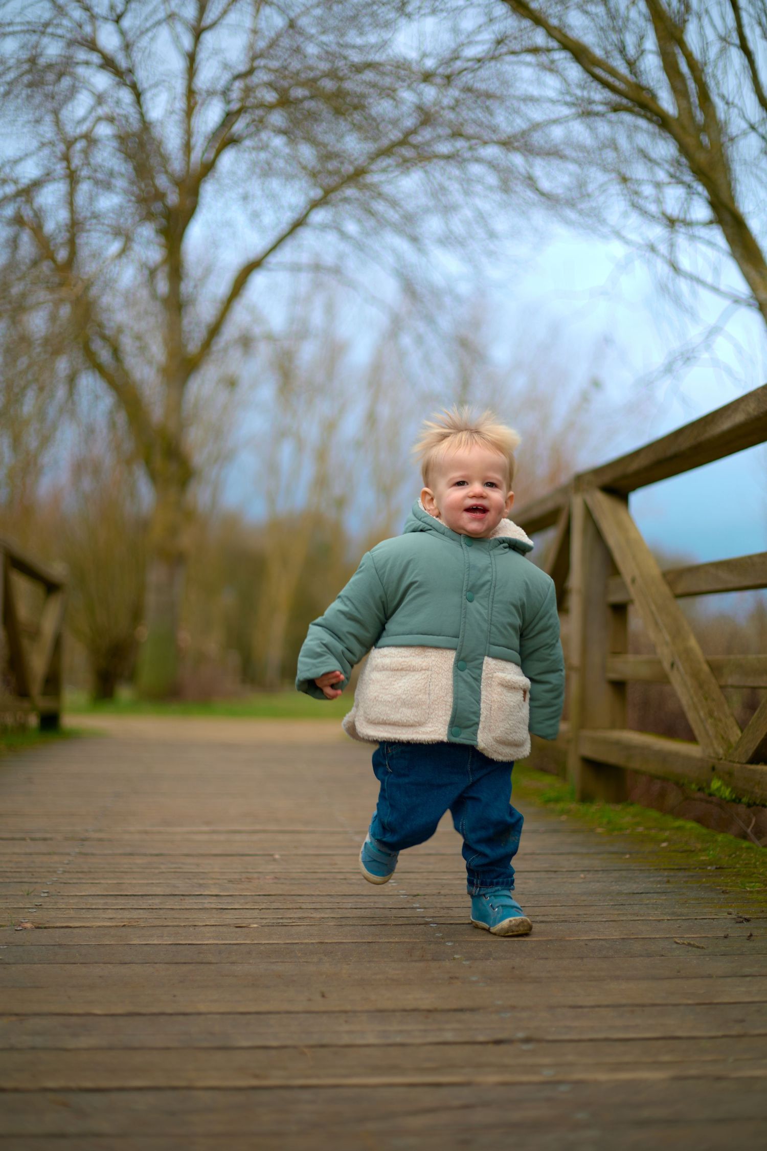 Small child walking and exploring on a wooden boardwalk surrounded by bare trees.