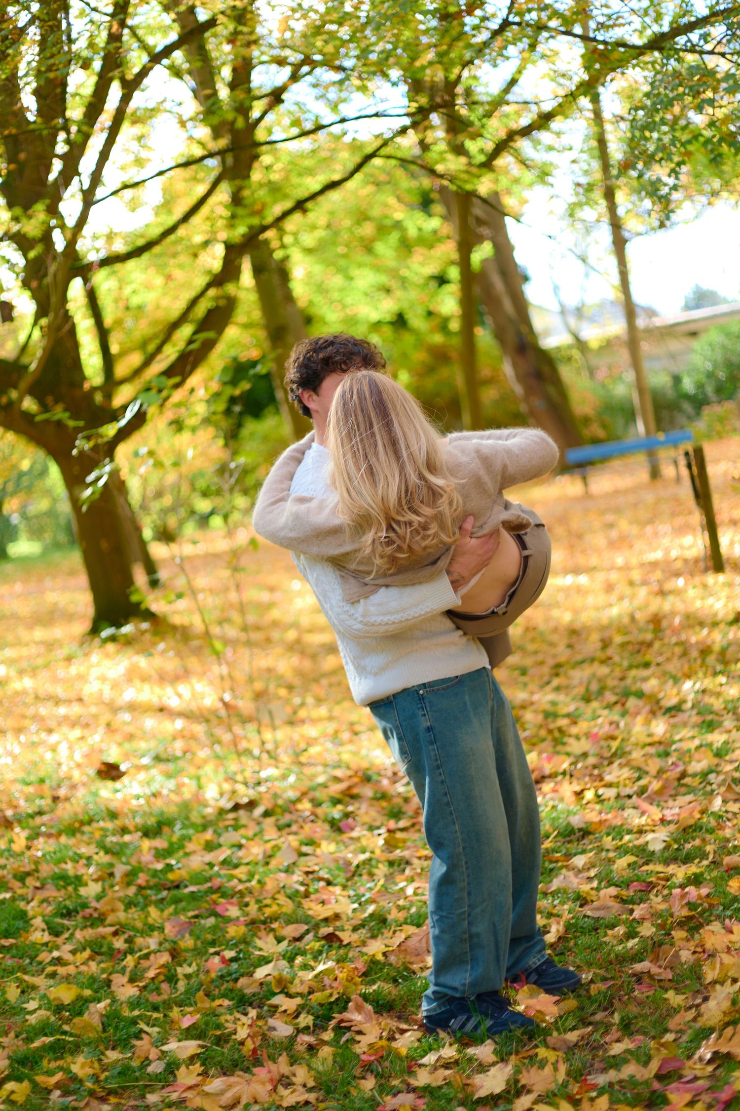 Couple embracing in autumn forest with fallen leaves on ground.