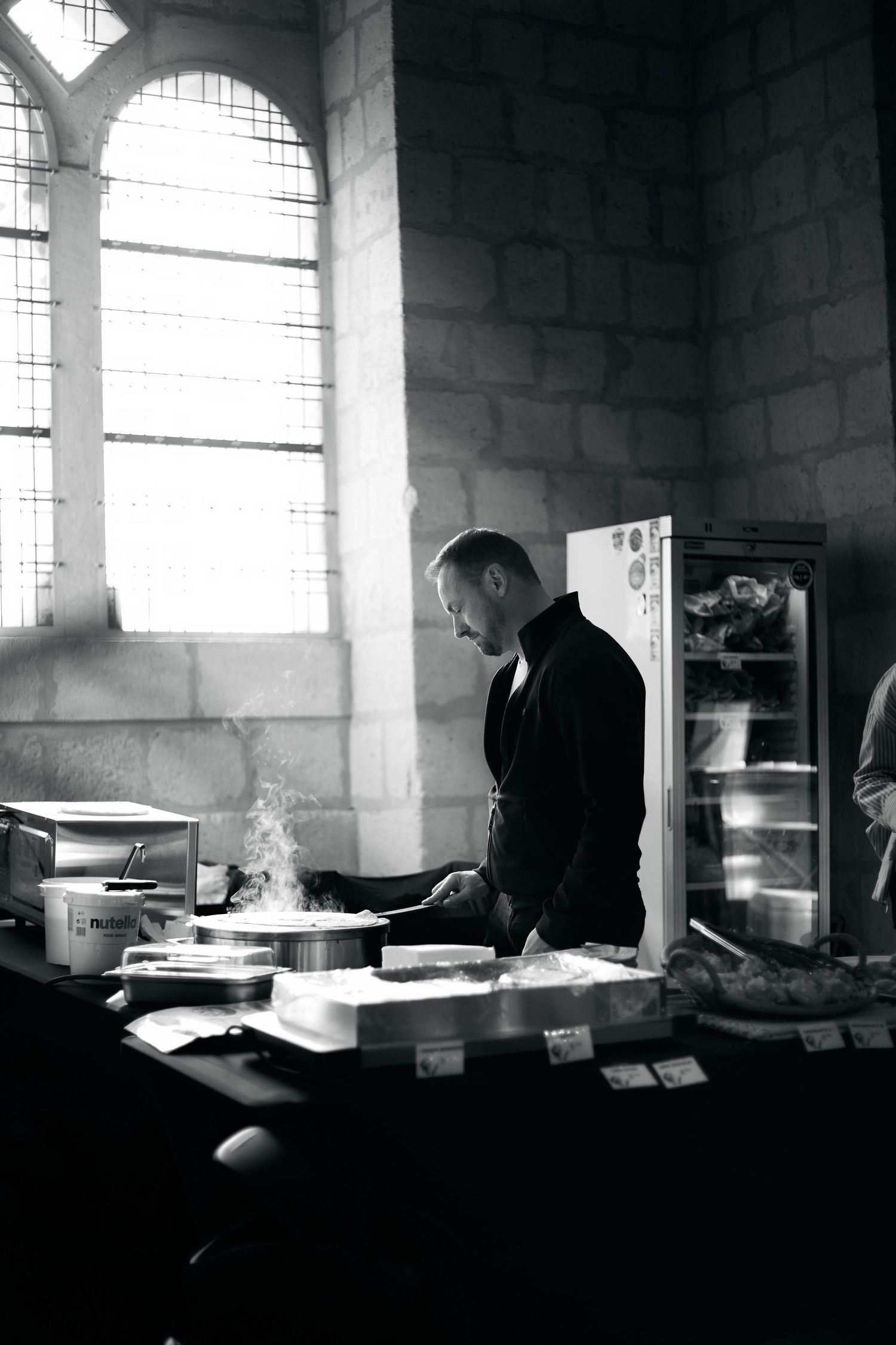 Dark moody interior scene with figure silhouetted against arched windows.