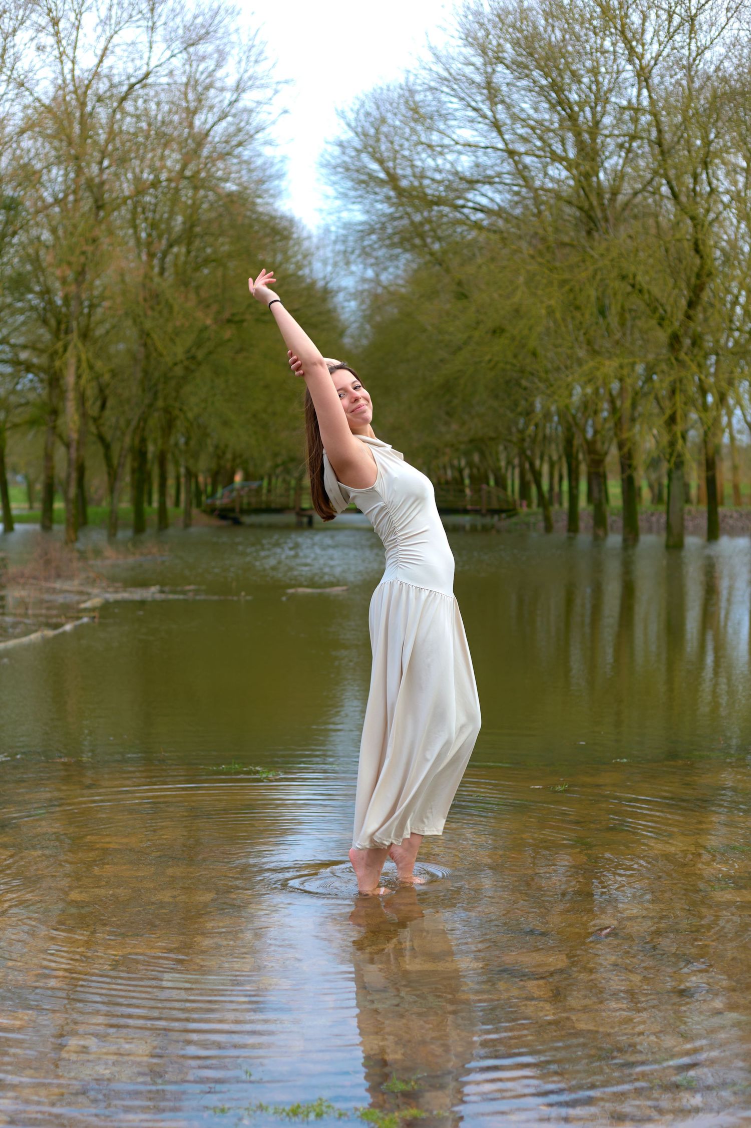 Expressive dance-like pose in white dress while standing in shallow flood waters.