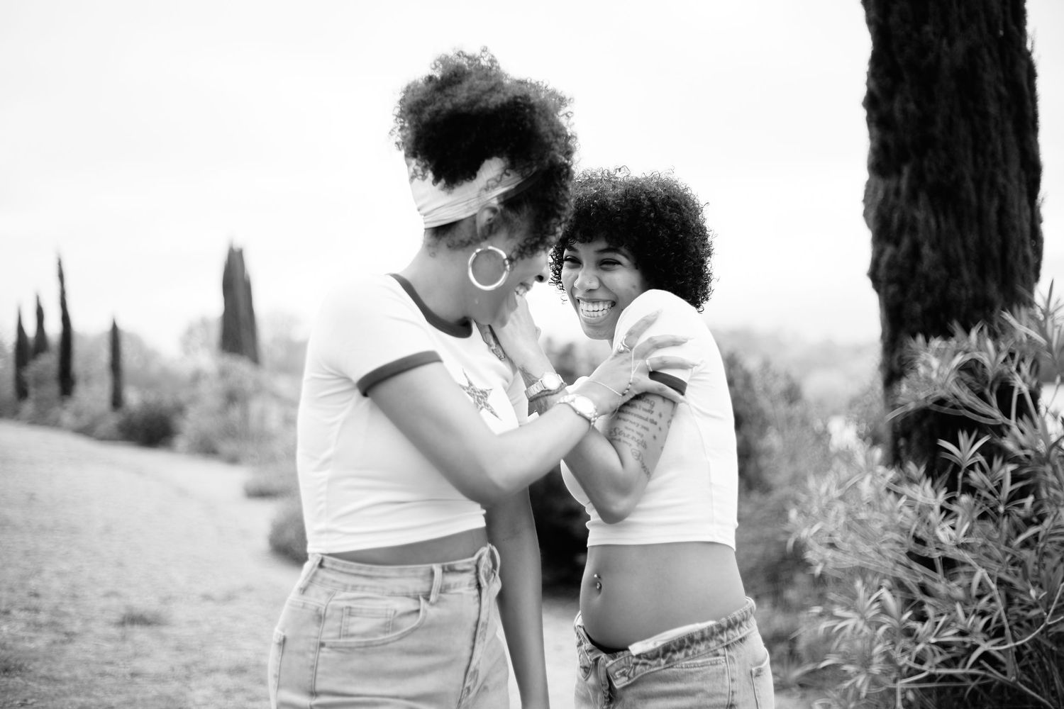 Two young women with natural curly hair share a joyful moment outdoors in a black and white photo.