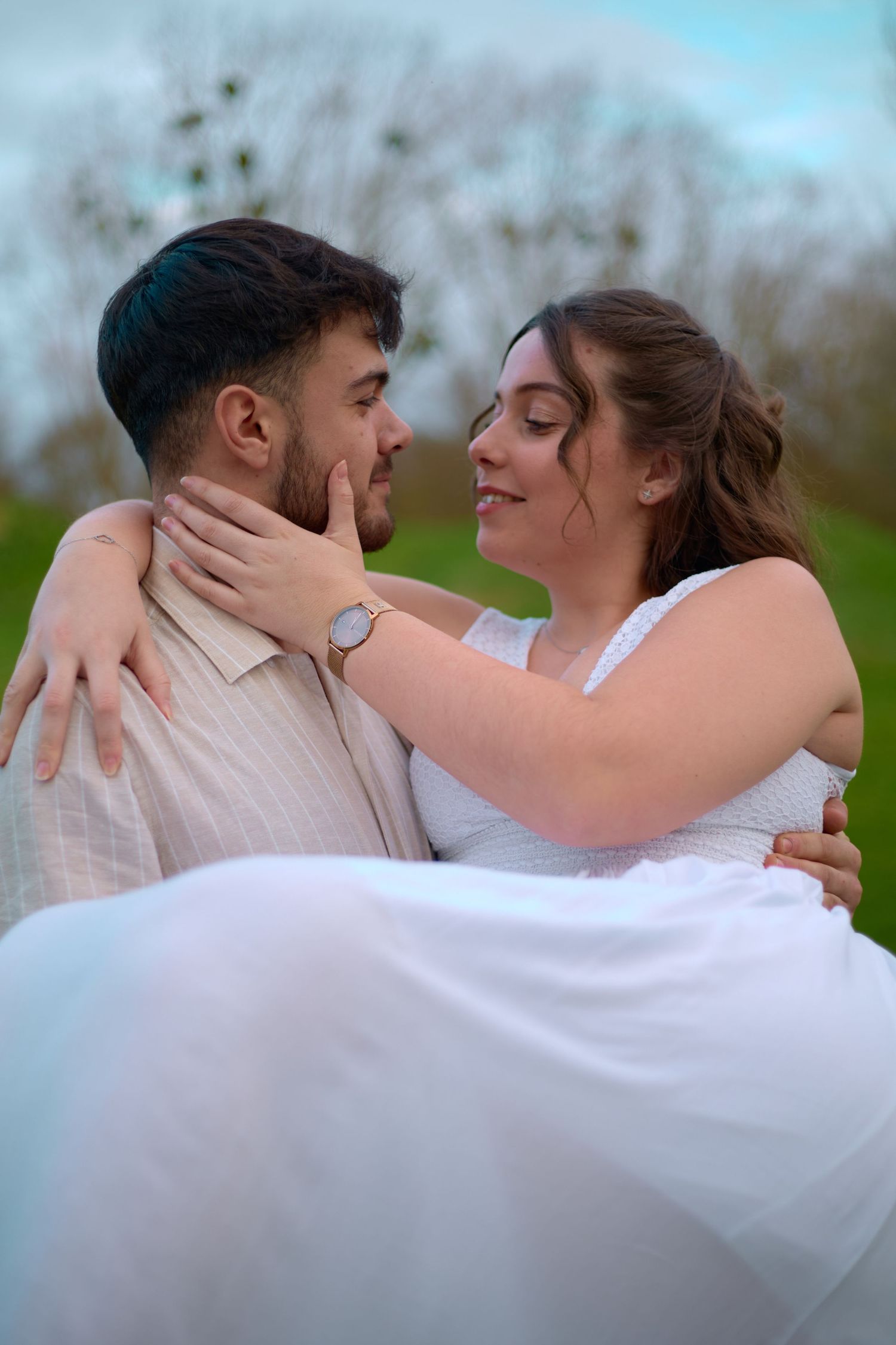 Romantic couple embracing outdoors with person in white dress being carried.