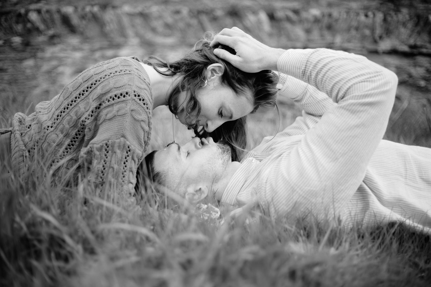 Black and white photo of a romantic couple lying in grass, gazing at each other tenderly.