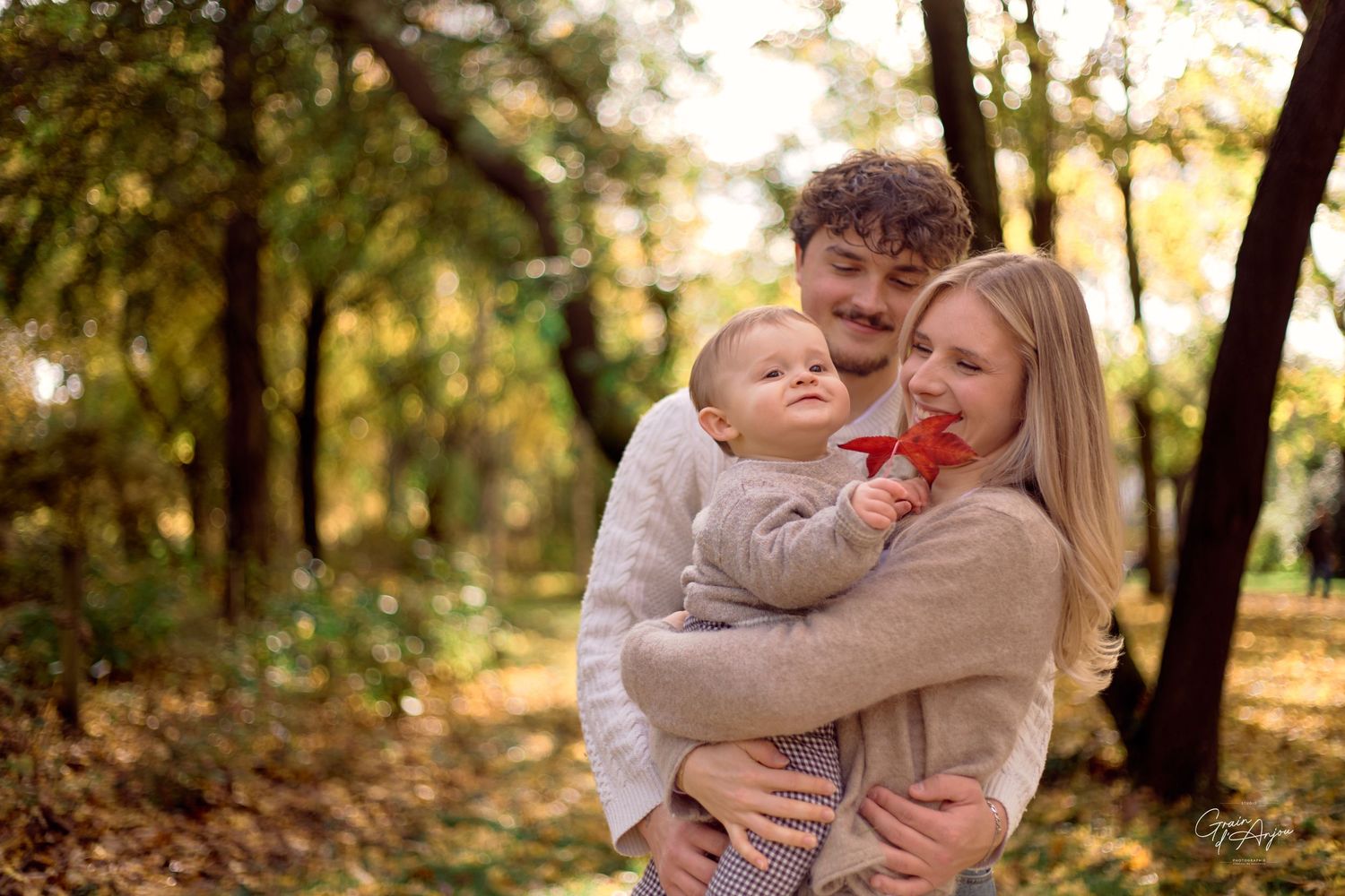 A family shares tender moments together on an autumn day in a wooded park setting.