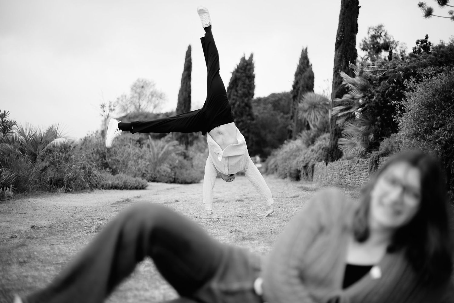 Black and white photo of person doing a cartwheel outdoors while a woman sits on grass in the foreground.