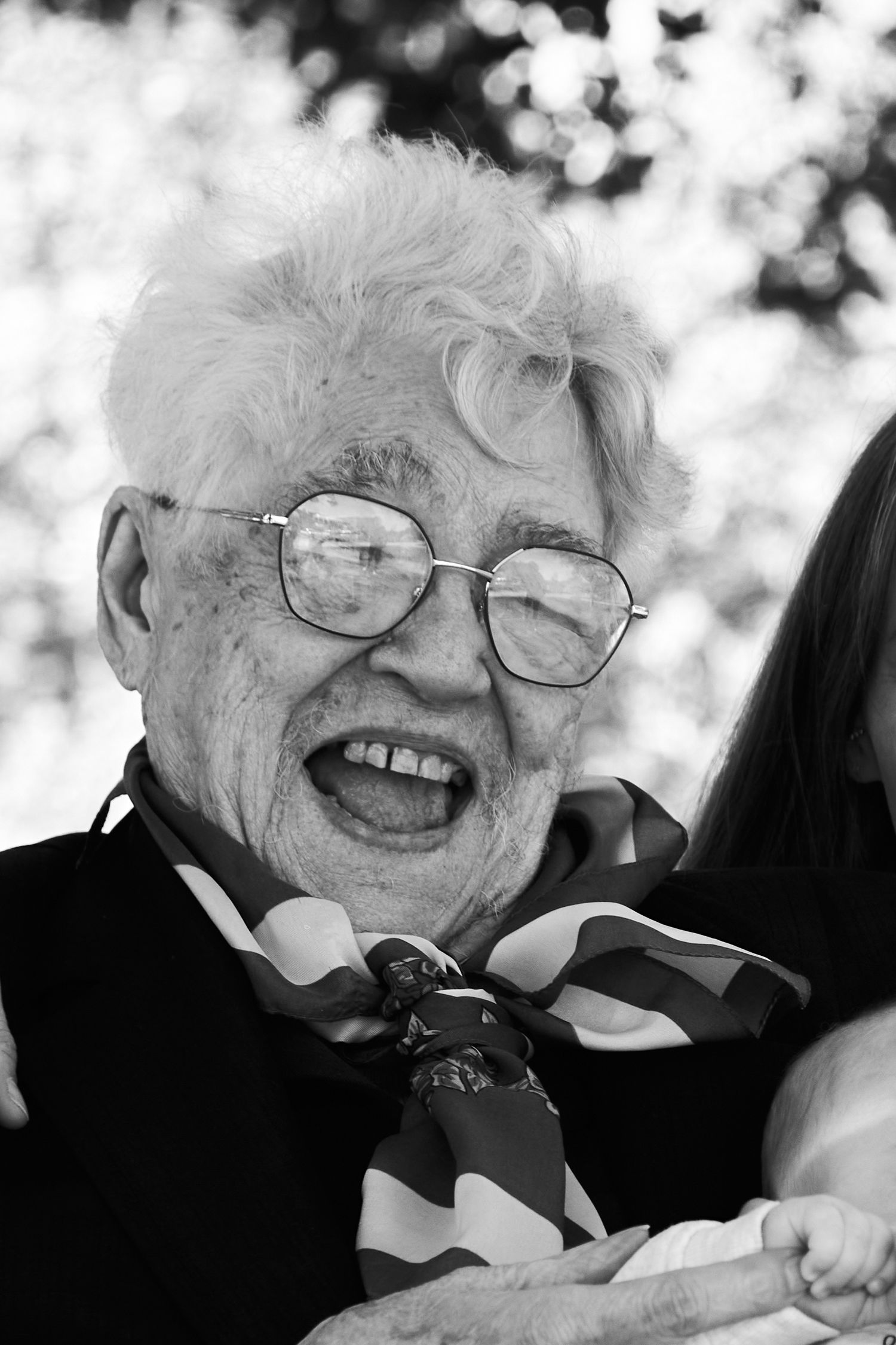 Elderly person wearing glasses laughs joyfully in black and white portrait.
