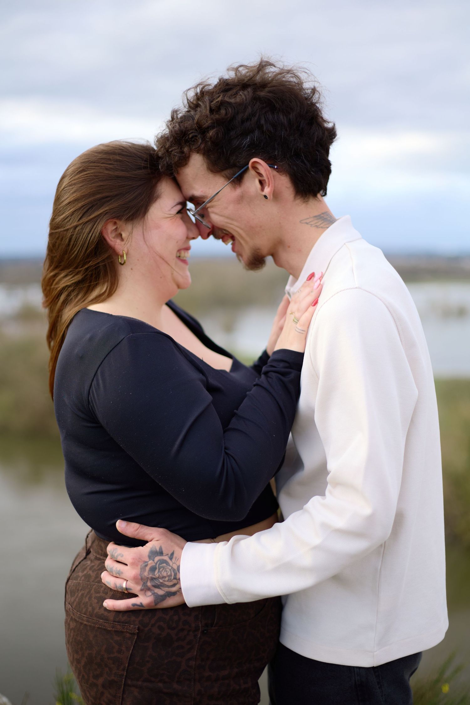 An intimate moment shared between two people in casual wear against a waterfront backdrop.