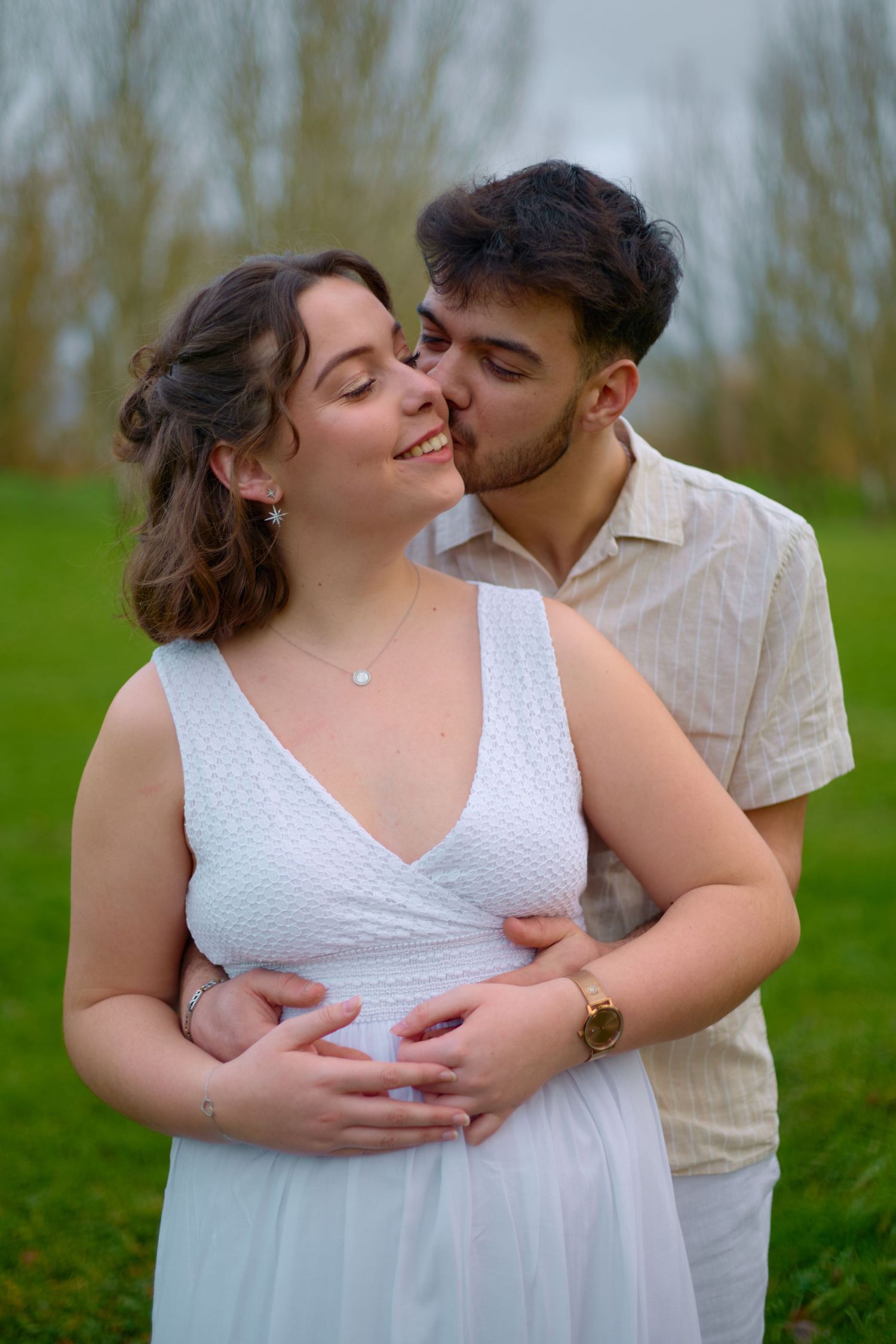 A romantic embrace captured outdoors with a couple in white and beige attire.