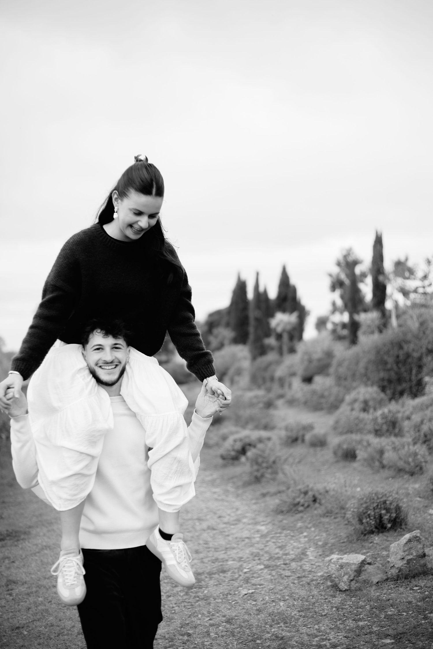 Black and white photo of a smiling woman sitting on a man's shoulders outdoors, both laughing joyfully.