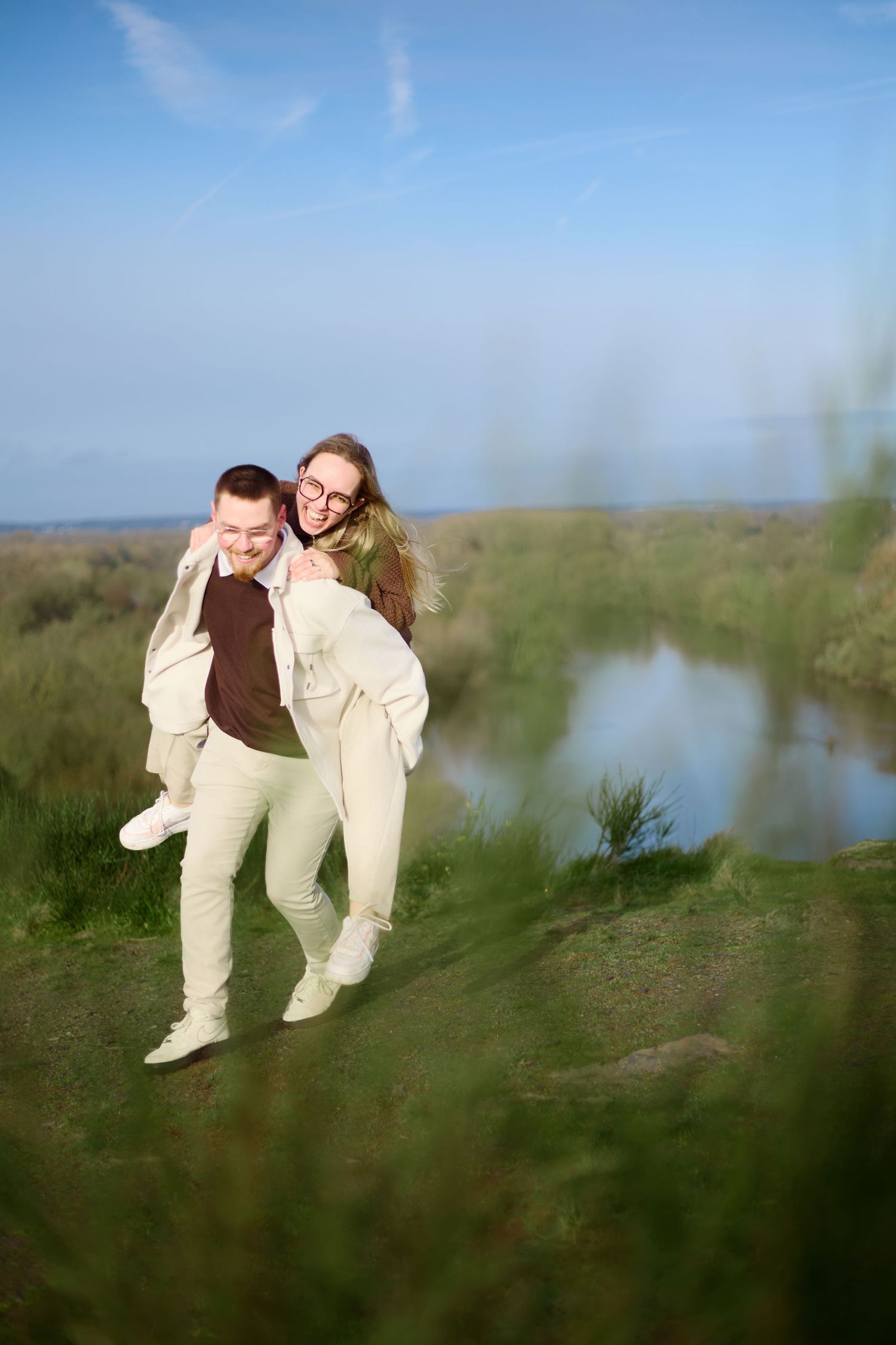 A playful piggyback ride moment between a couple in light colored clothing by a scenic river.