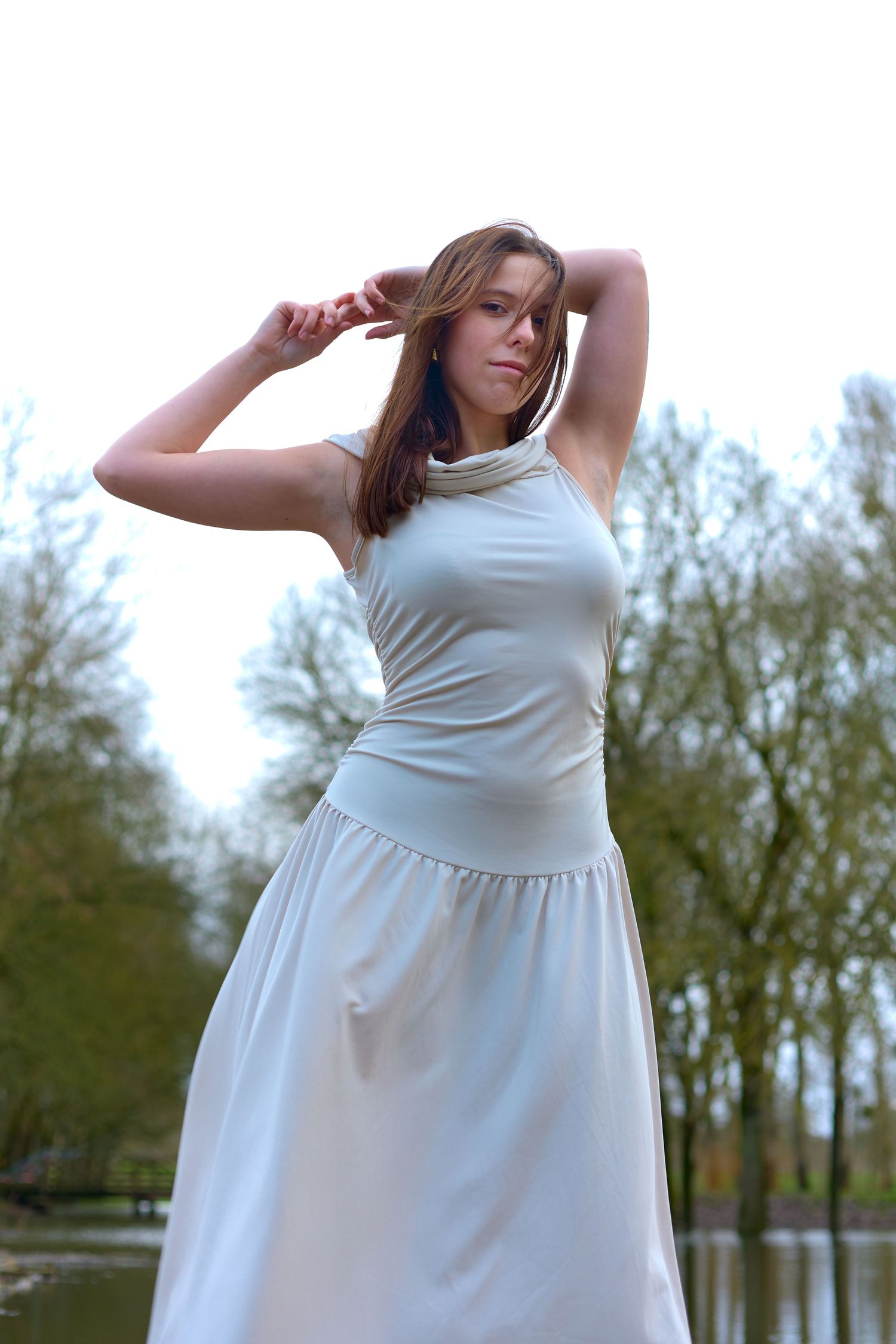 Graceful pose in flowing white dress against natural water backdrop.