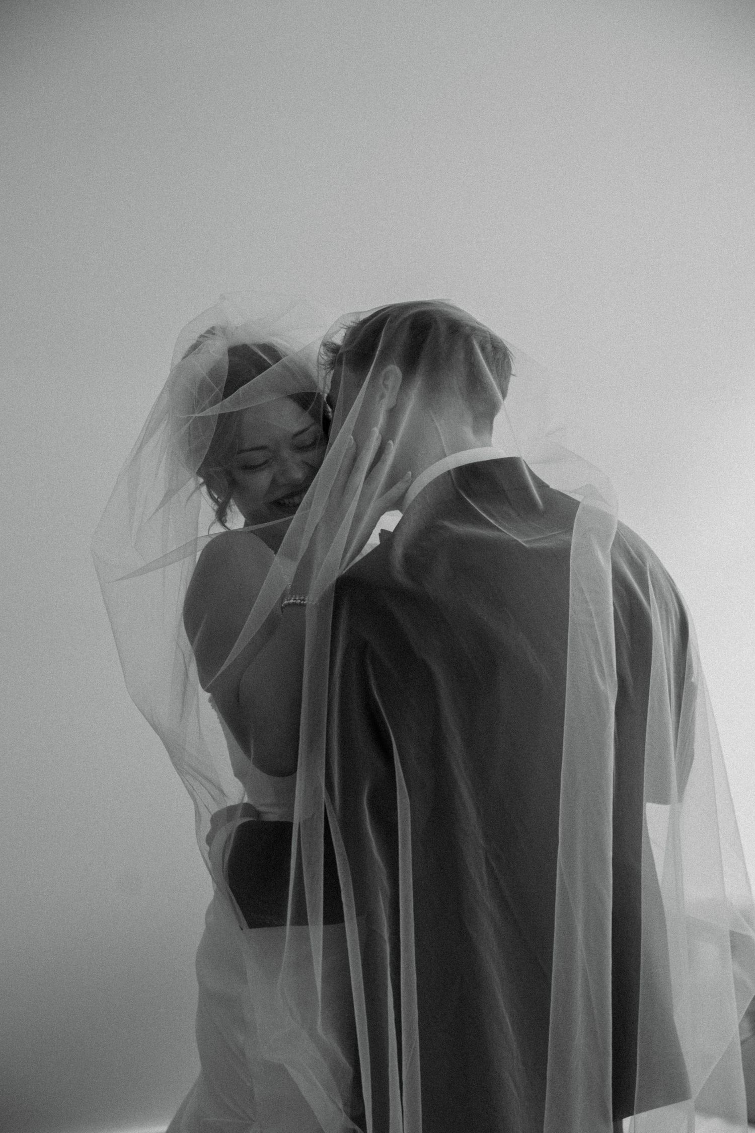 Black and white photo of a couple sharing an intimate moment beneath a flowing bridal veil.