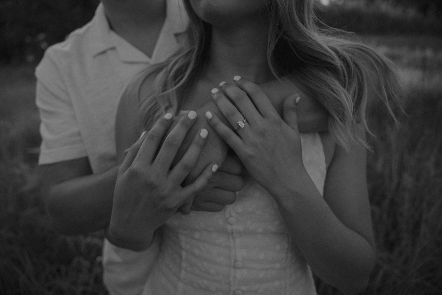 Black and white photo of a couple holding hands over the woman's heart, showcasing engagement rings.
