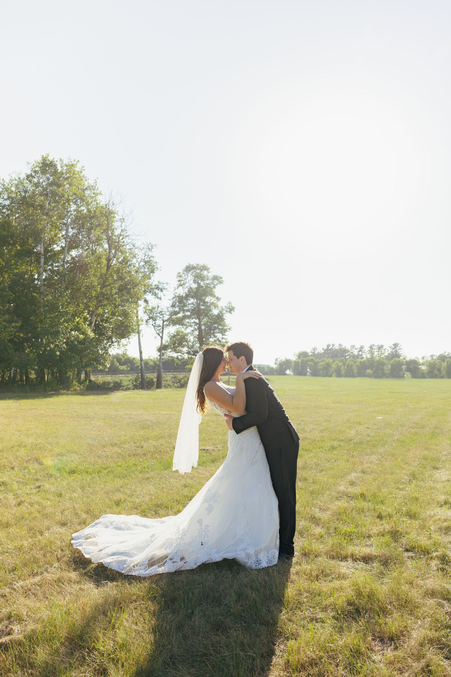 Bride and groom sharing a dip kiss in open green field on sunny day.