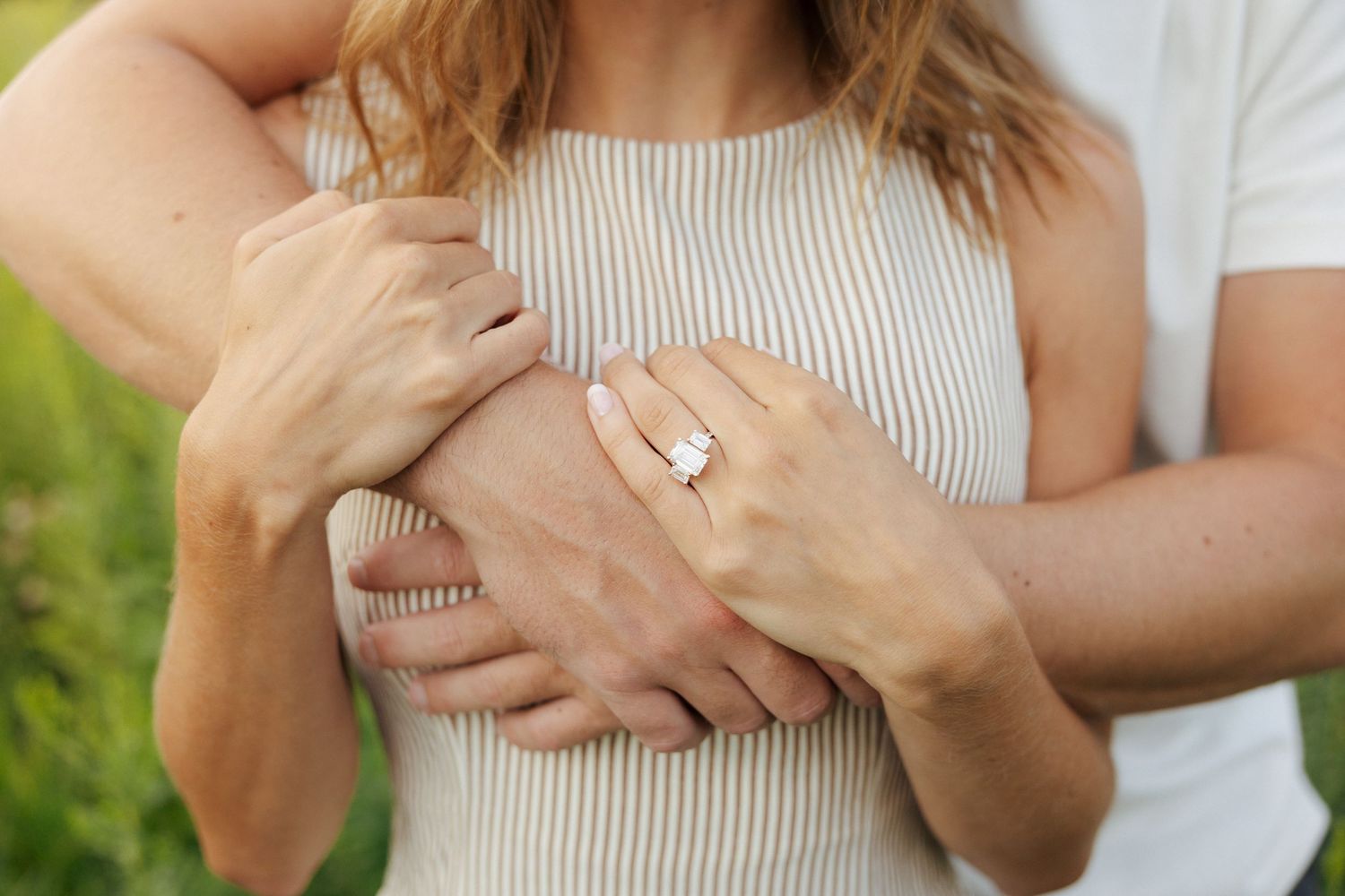 Couple embracing outdoors, woman displaying elegant diamond engagement ring on her finger.