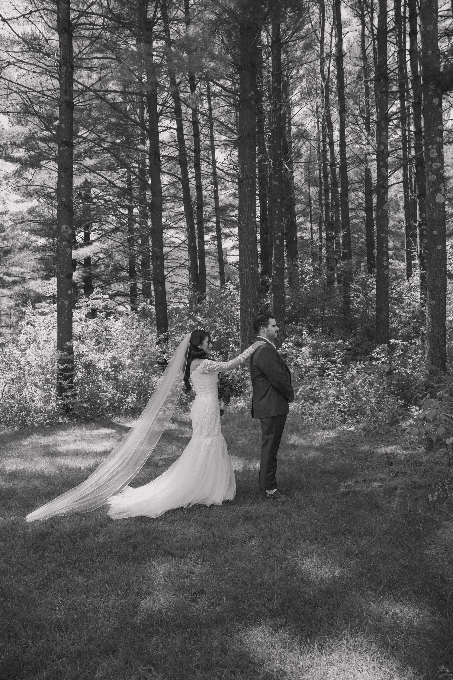 Bride and groom dance together in a sunlit forest clearing, her long veil flowing behind them.