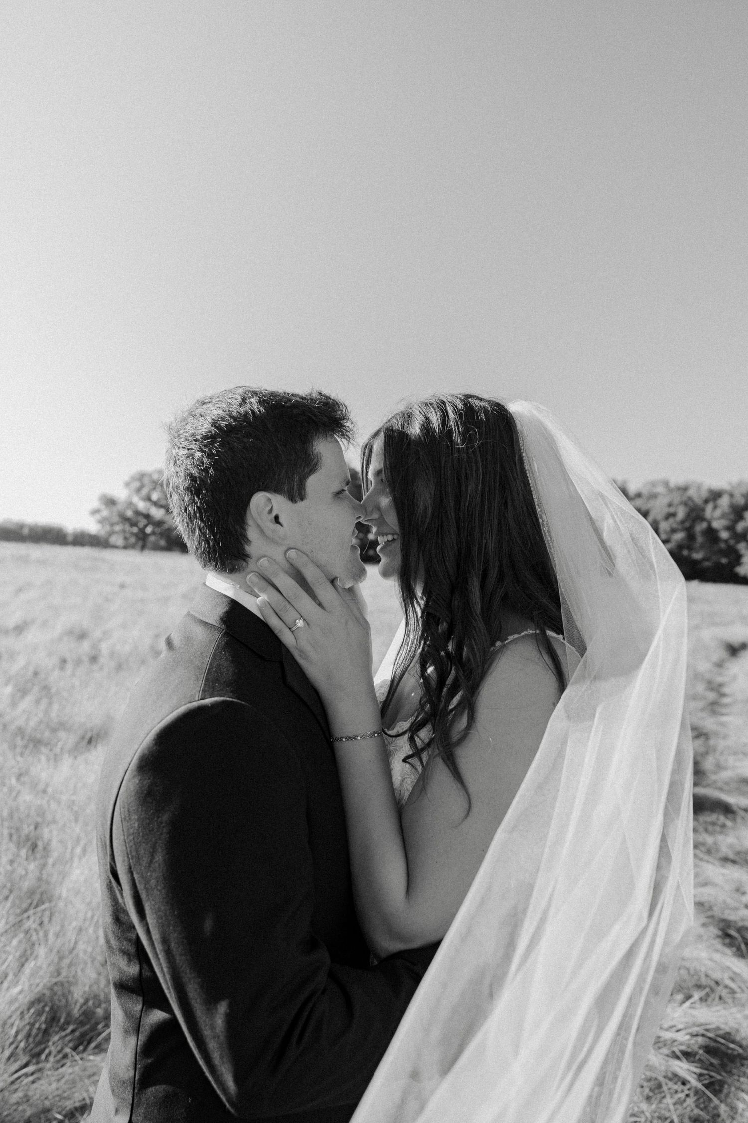 Black and white photo of bride and groom sharing intimate moment in open field.