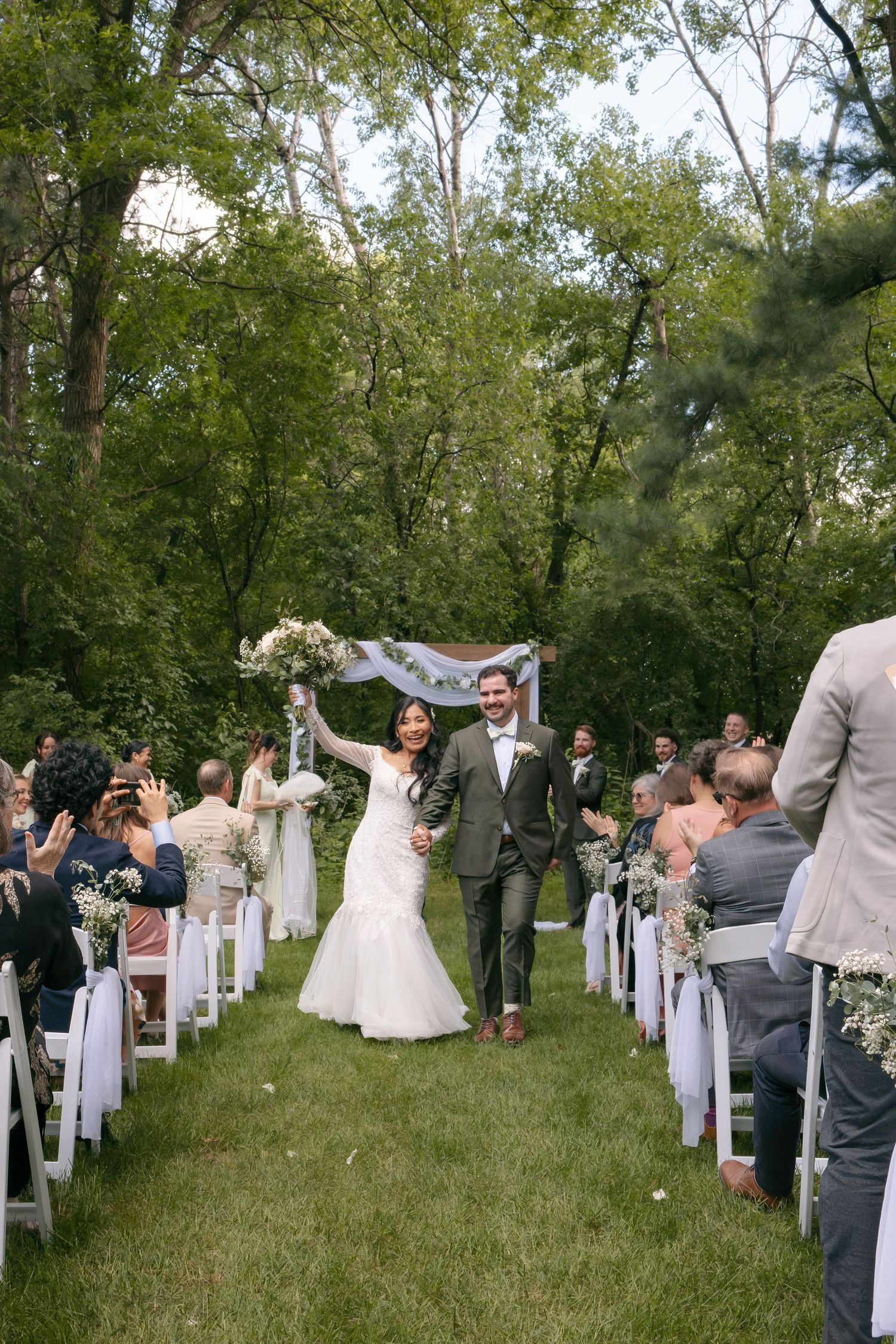 Newlyweds joyfully walk down outdoor aisle after ceremony as guests celebrate around them.