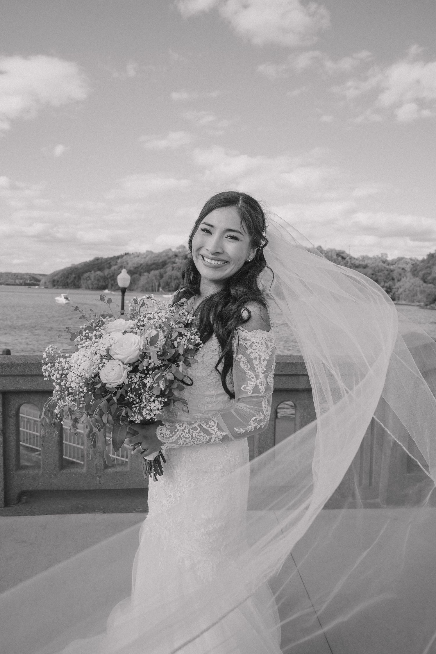 Black and white bride holding bouquet with veil flowing in wind outdoors.