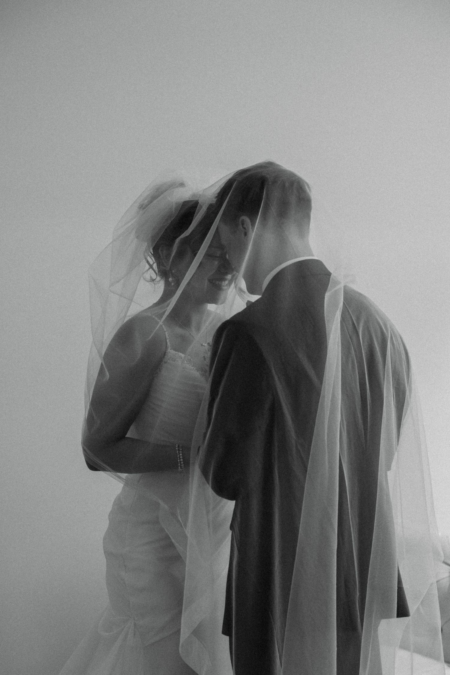Black and white photo of bride and groom sharing an intimate moment under a flowing veil on their wedding day.