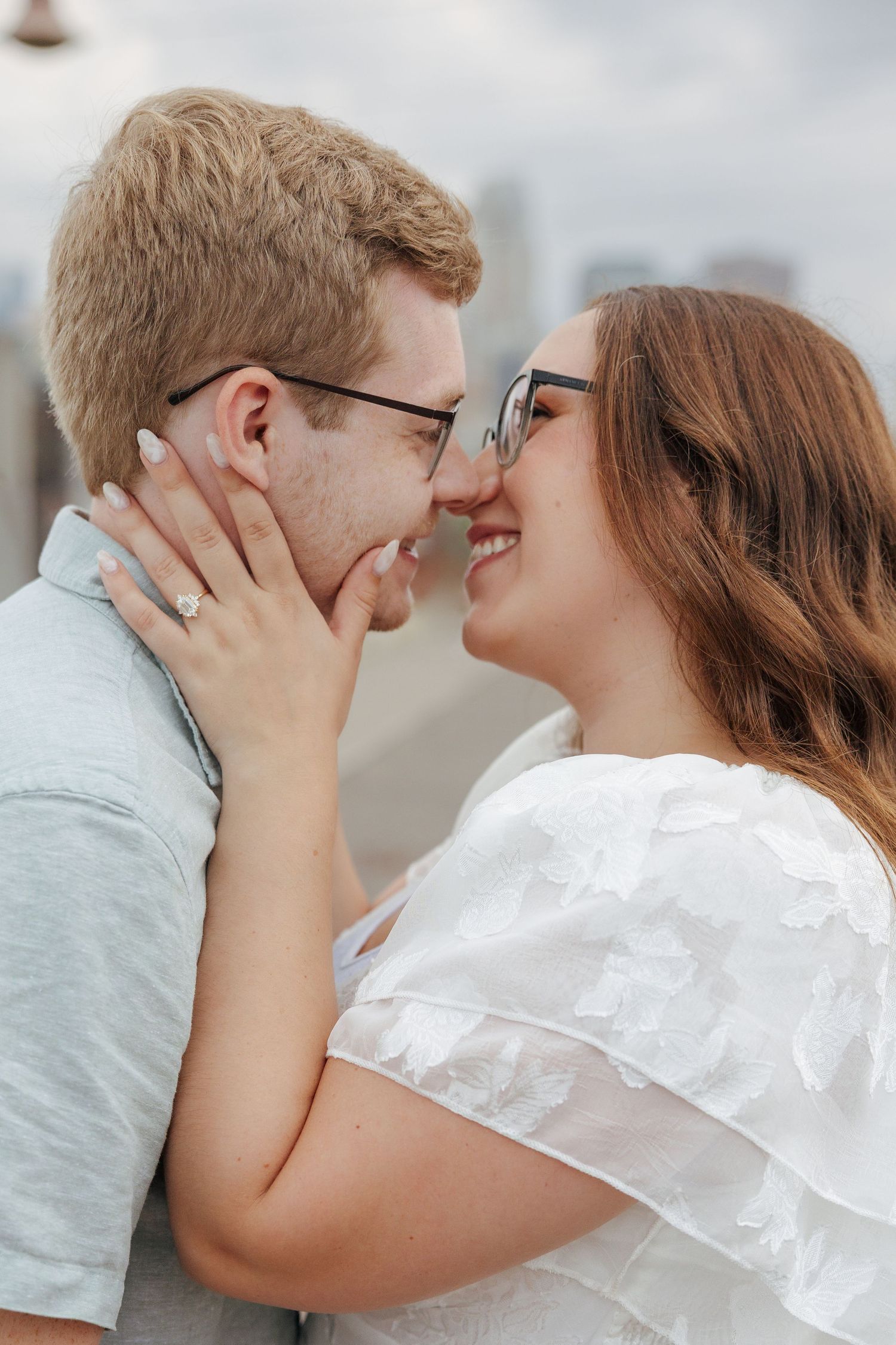 Romantic close-up of a smiling couple about to kiss, woman wearing an engagement ring outdoors.