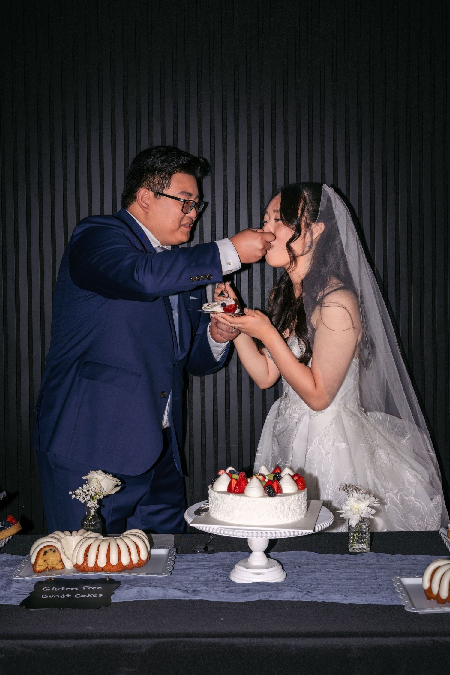 Bride and groom feeding each other wedding cake at reception table with strawberry decorated white cake.