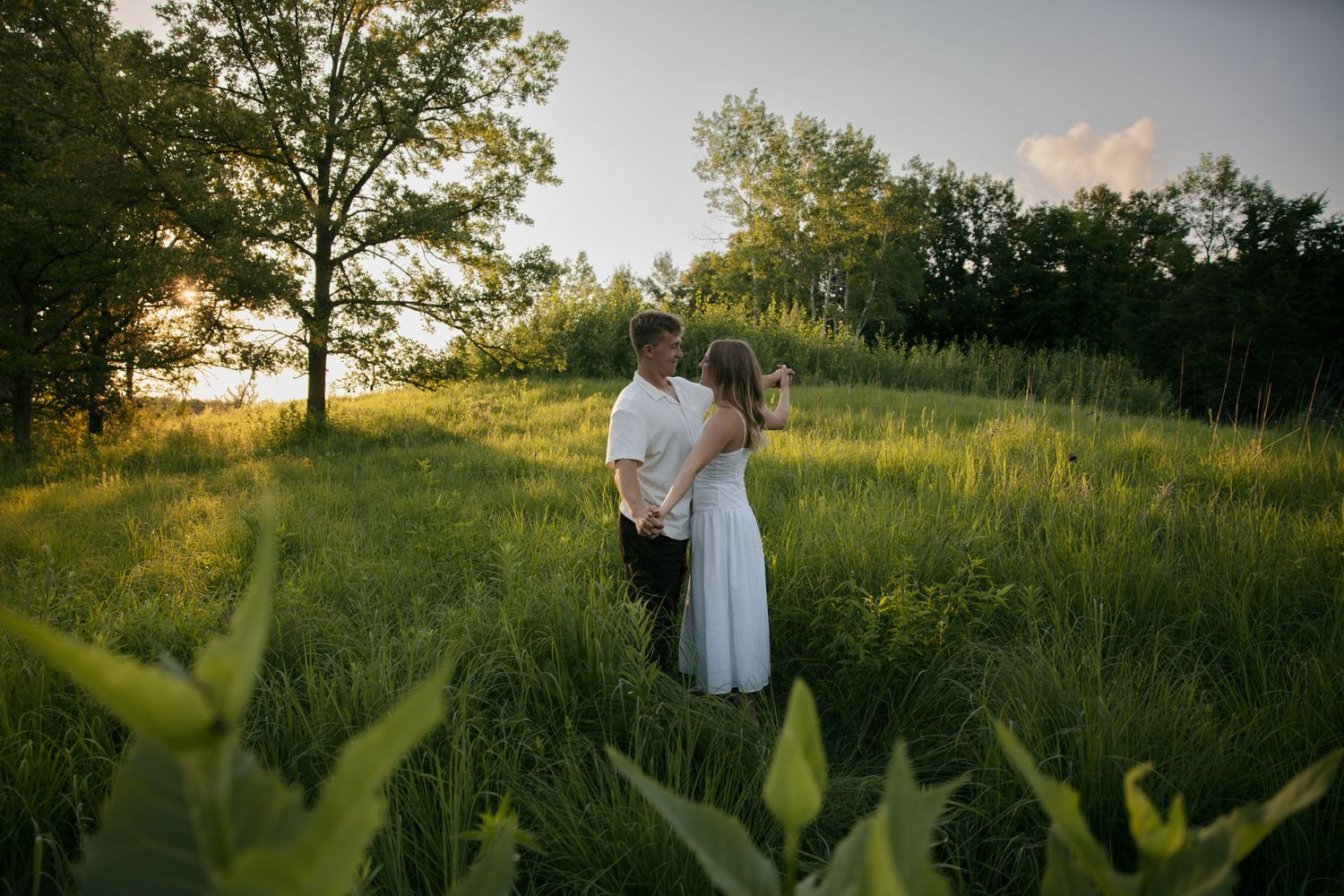 Couple embracing in a lush green meadow at golden hour with trees in the background.
