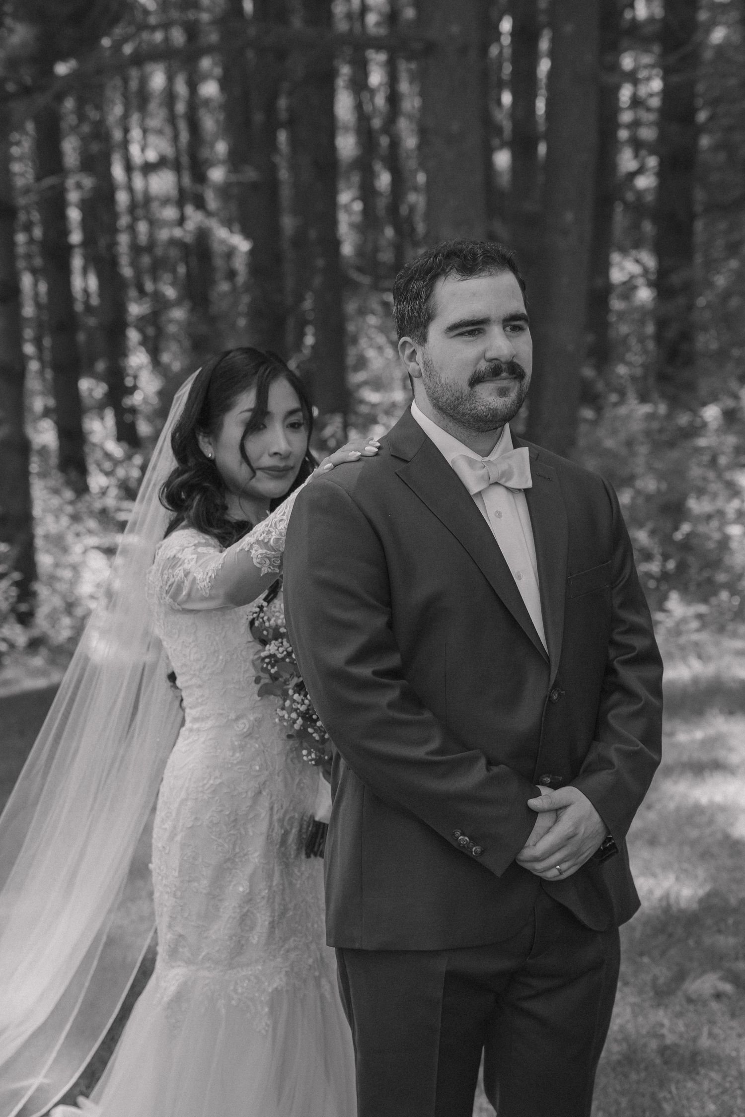 Black and white photo of bride and groom sharing first look in forest.