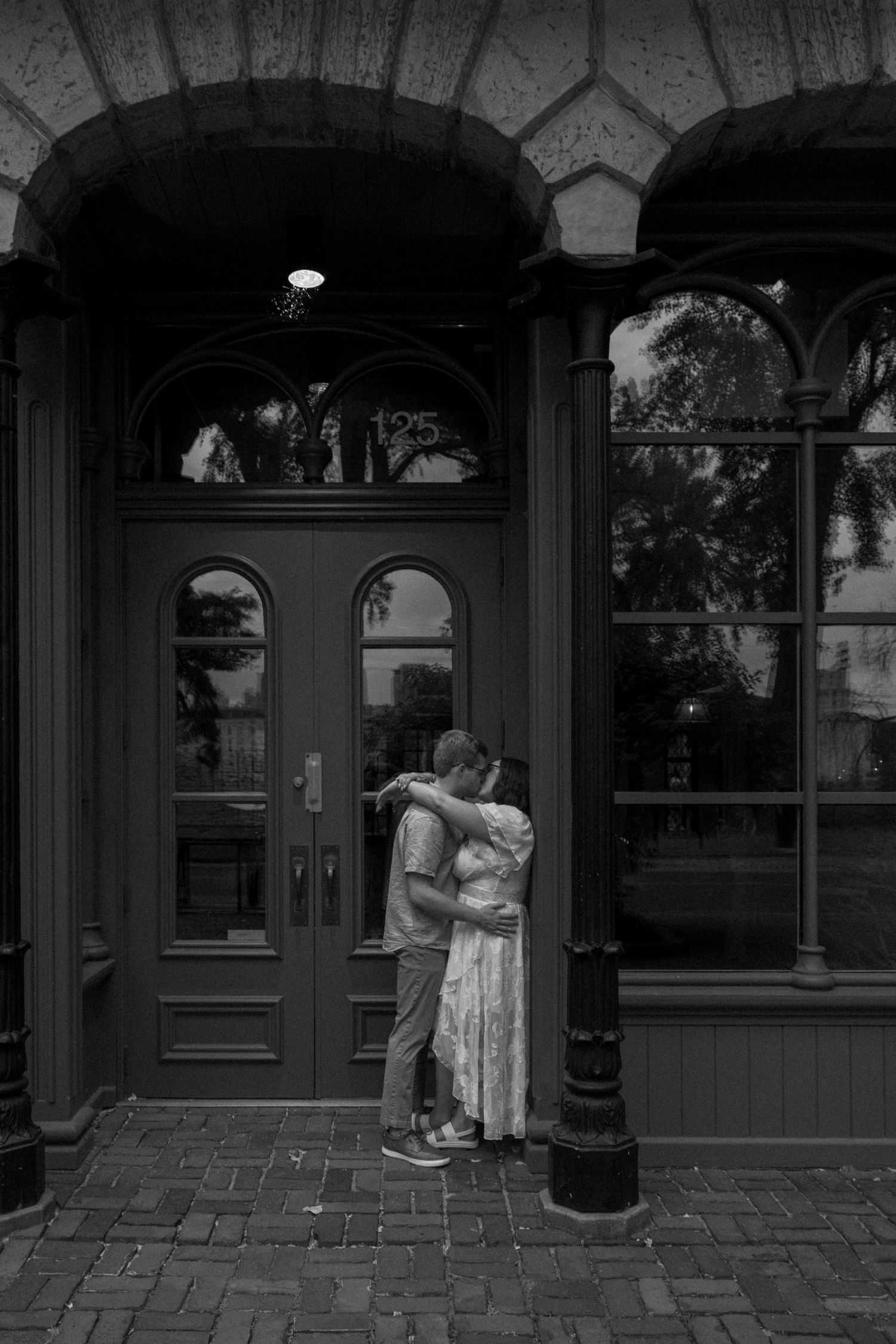Black and white photo of a couple embracing in a doorway of a historic building with ornate arched architecture.