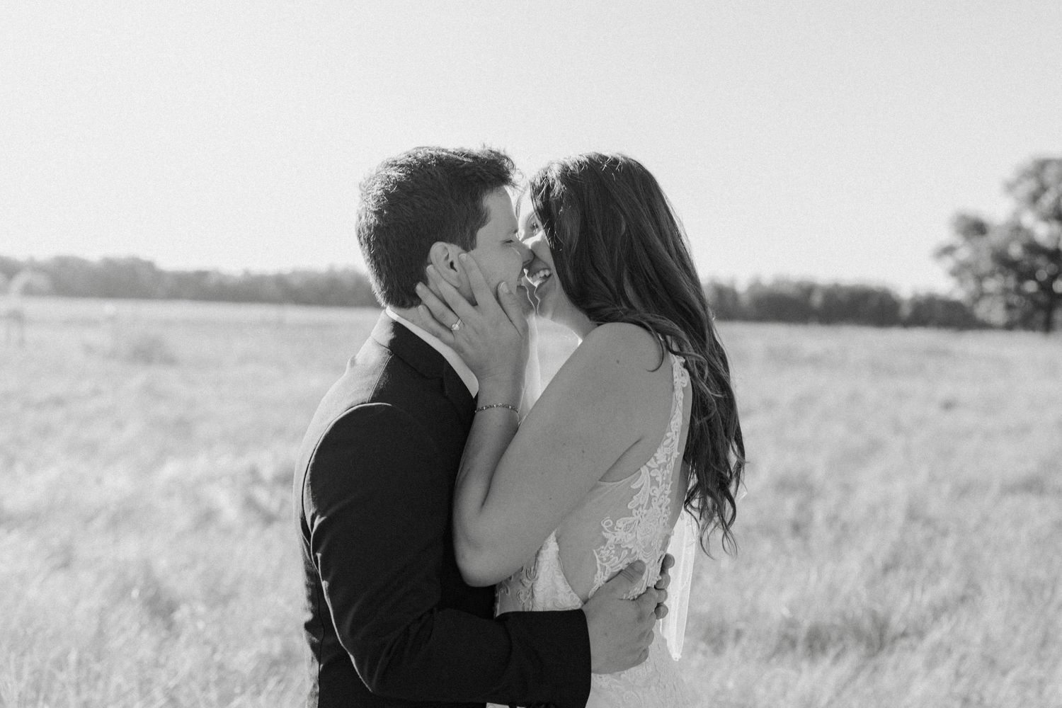 Black and white photo of bride and groom sharing a romantic kiss in an open field.