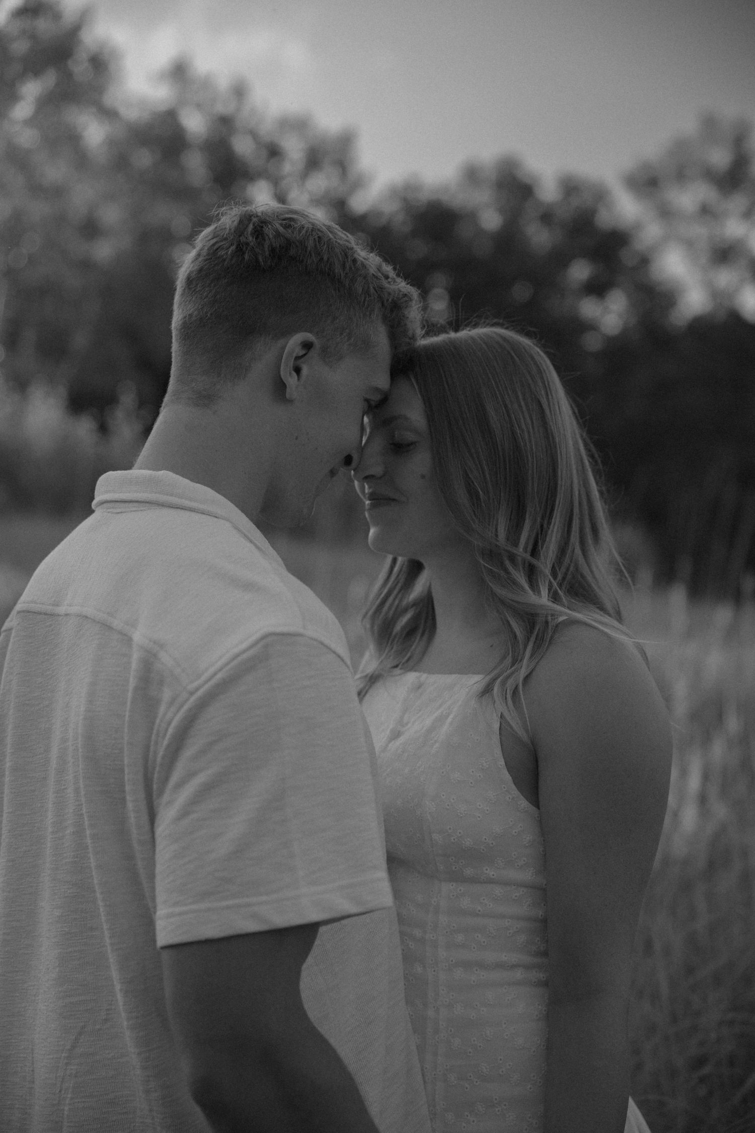 Black and white photo of a couple sharing an intimate moment, foreheads touching in a field.