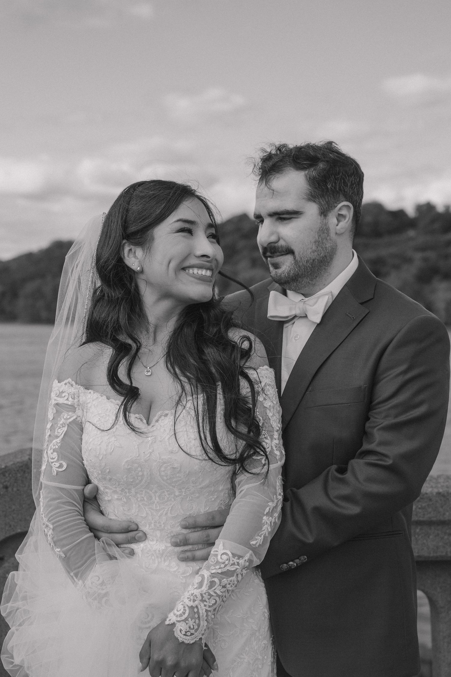 Black and white portrait of smiling bride in lace dress and groom in suit sharing a tender moment.