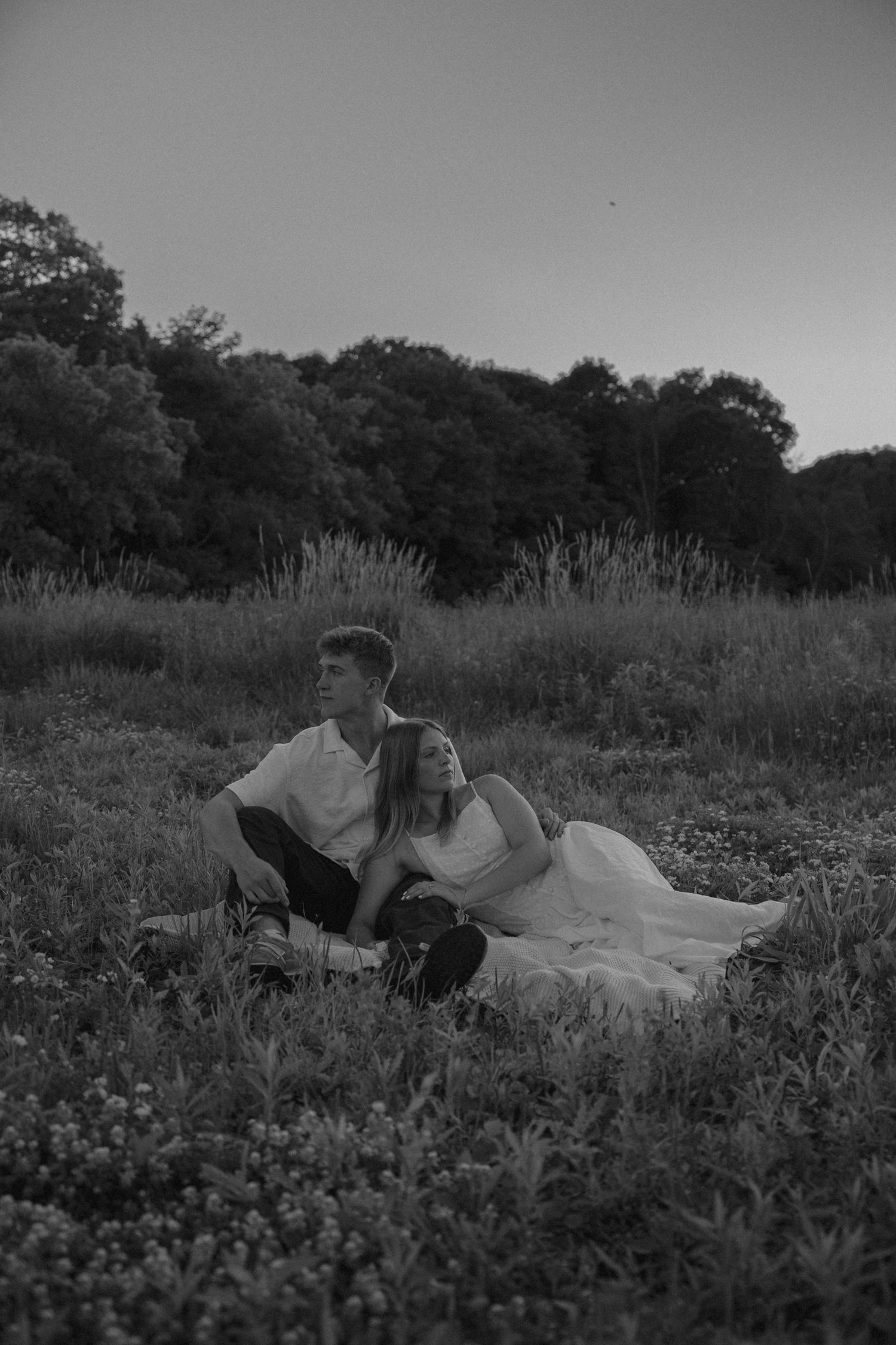 Black and white romantic photo of a couple relaxing together in a grassy field at twilight.
