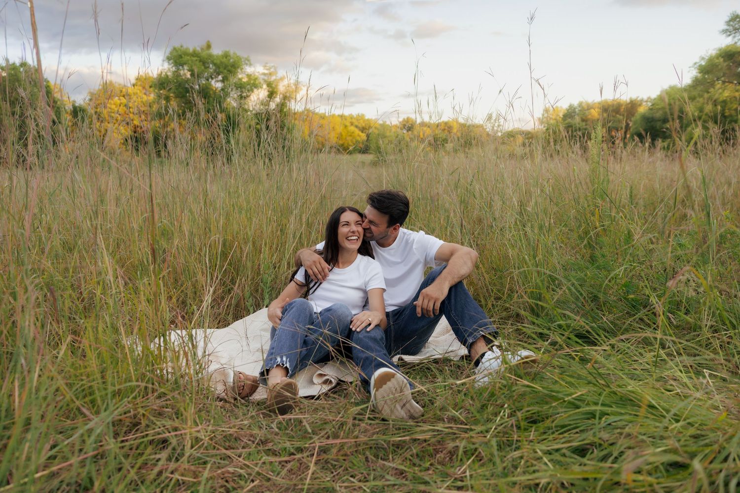 Couple sitting together on a blanket in a lush green field, sharing a romantic moment outdoors.