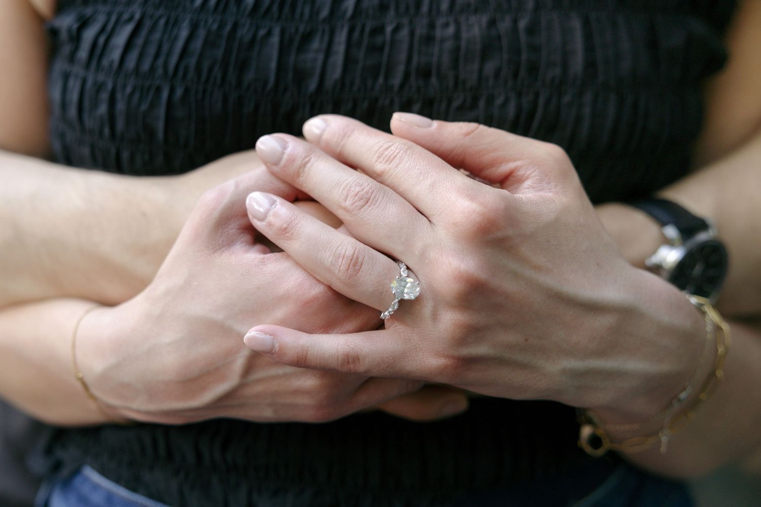 Close-up of couple holding hands showing diamond engagement ring and bracelet.