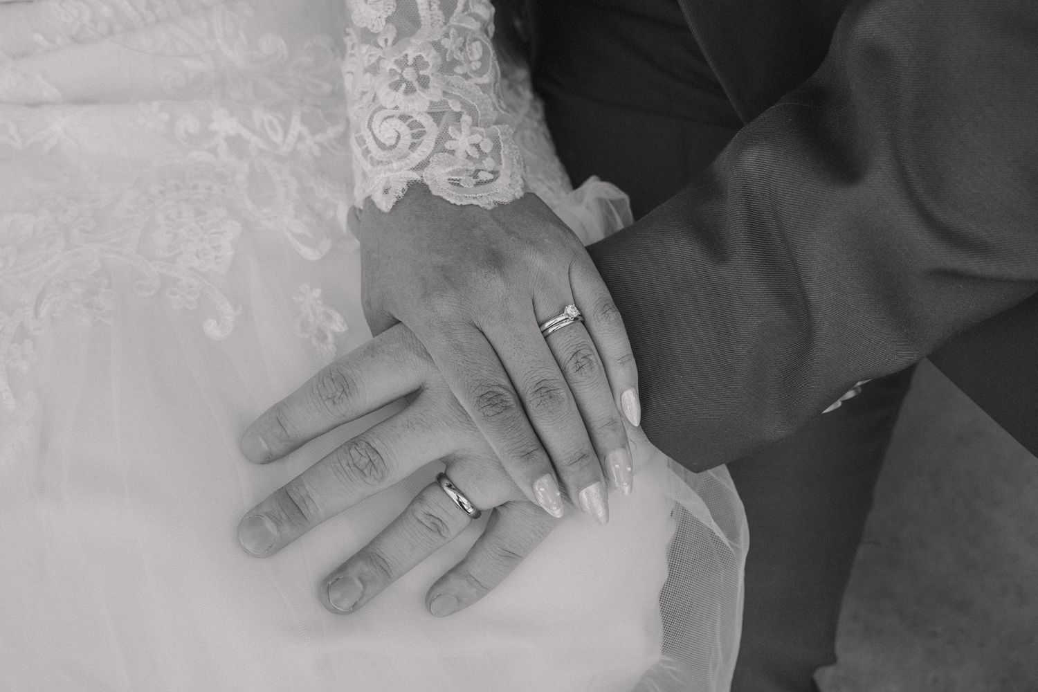 Black and white photo of newlyweds hands showing wedding rings on their fingers.