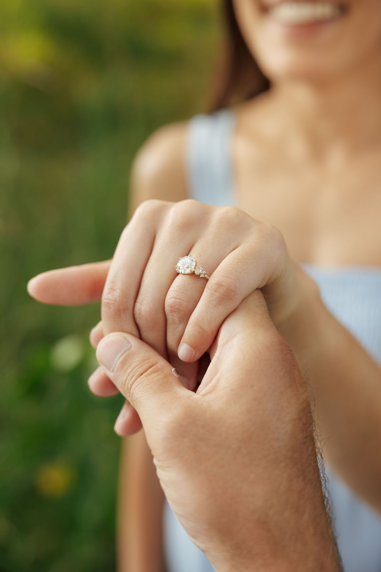 Close-up of a man placing a diamond engagement ring on a smiling woman's finger outdoors.