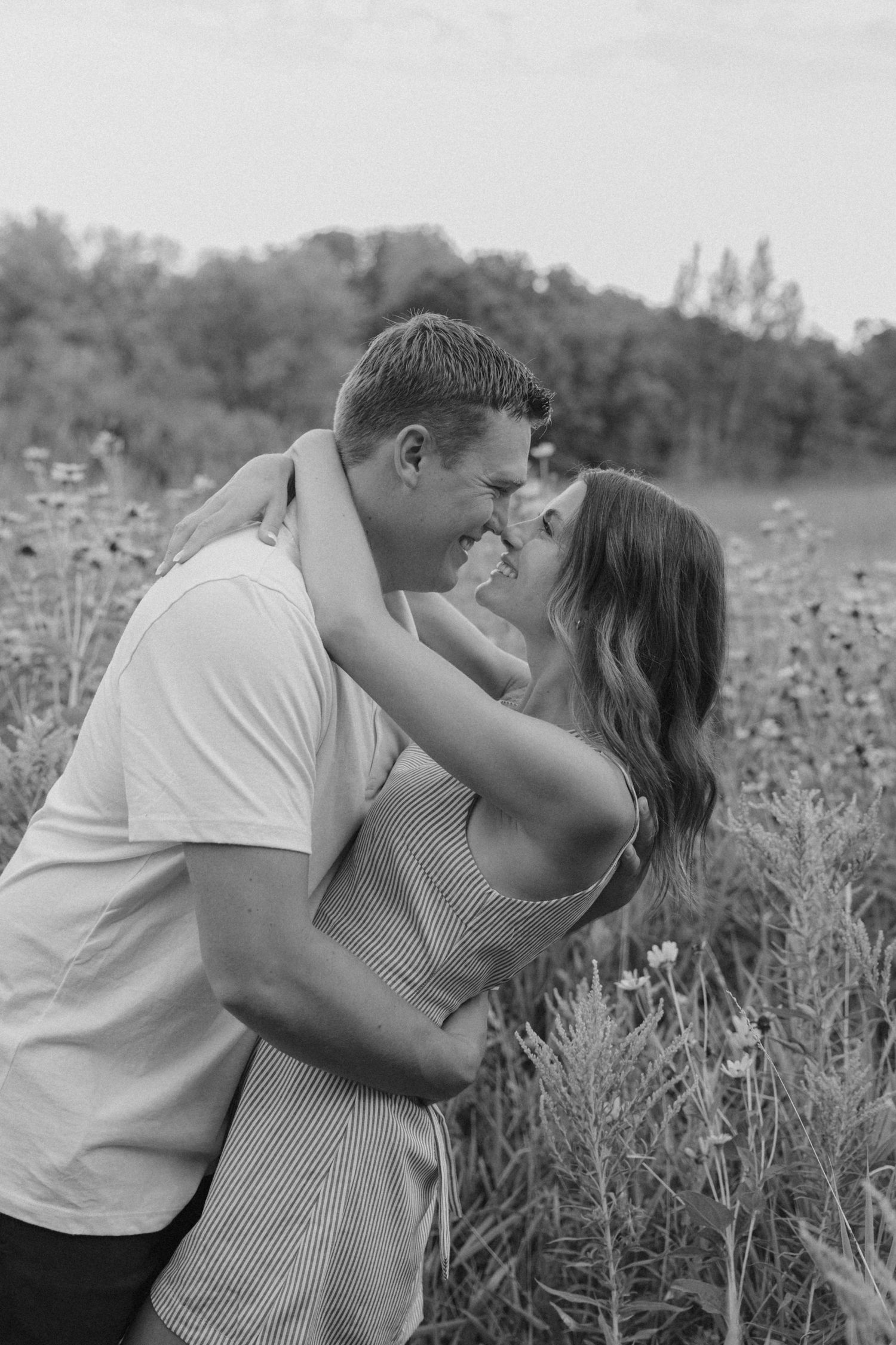 Black and white photo of a couple embracing and smiling at each other in a wildflower field.