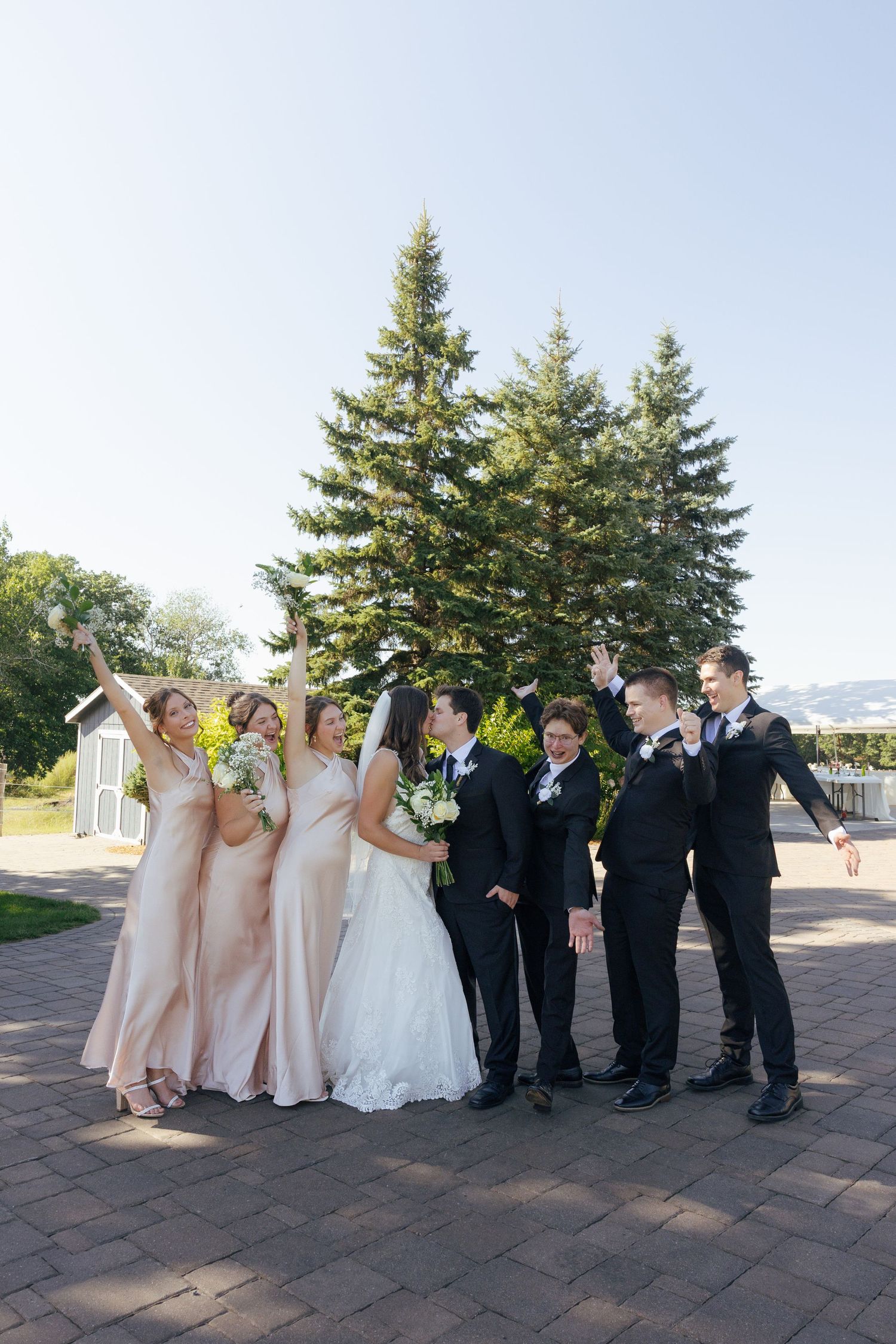 Wedding party celebrating outdoors with bride, groom, bridesmaids and groomsmen cheering.
