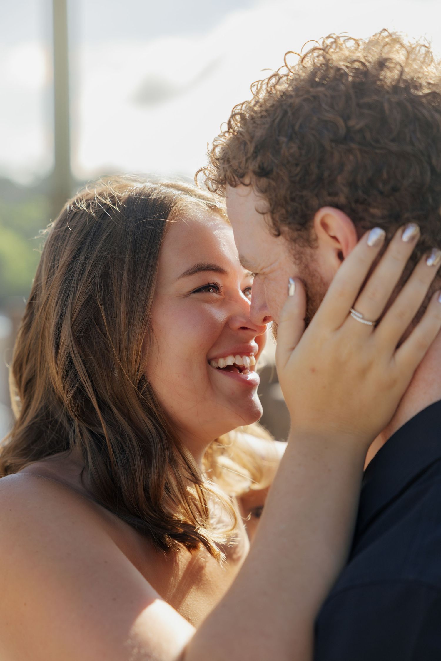 A joyful couple shares a romantic moment, the woman smiling brightly while wearing a diamond ring on her hand.