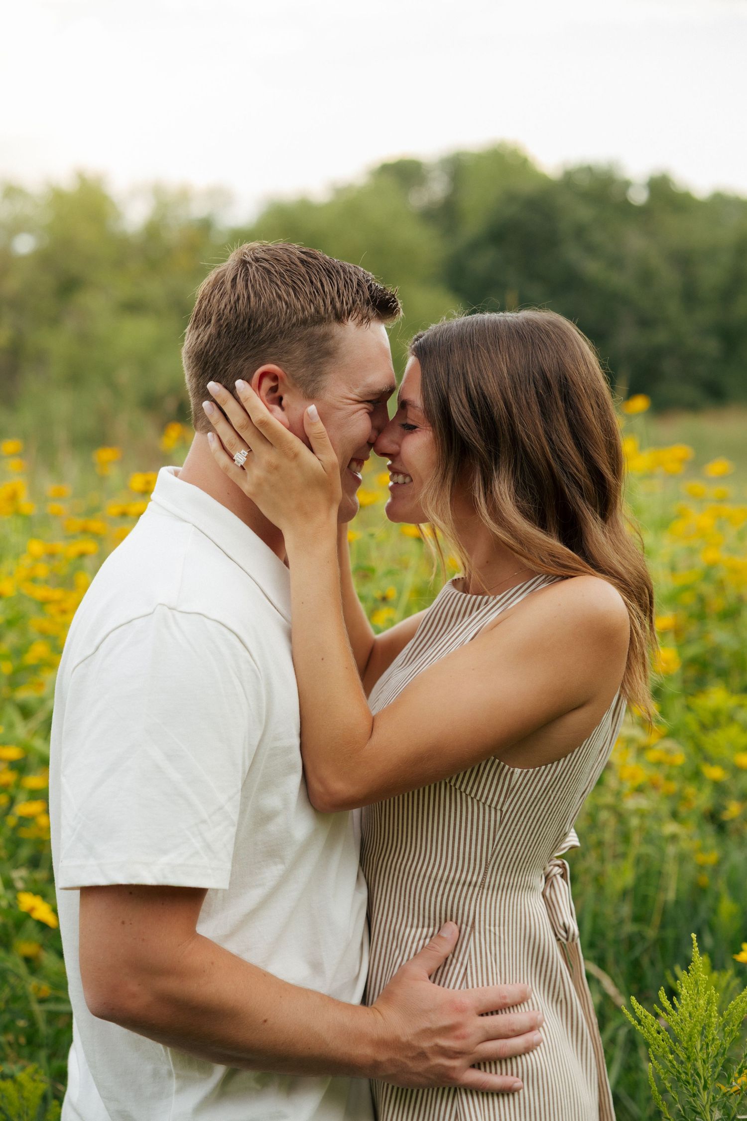 Couple sharing a romantic almost-kiss in a sunflower field, woman touching mans face tenderly.