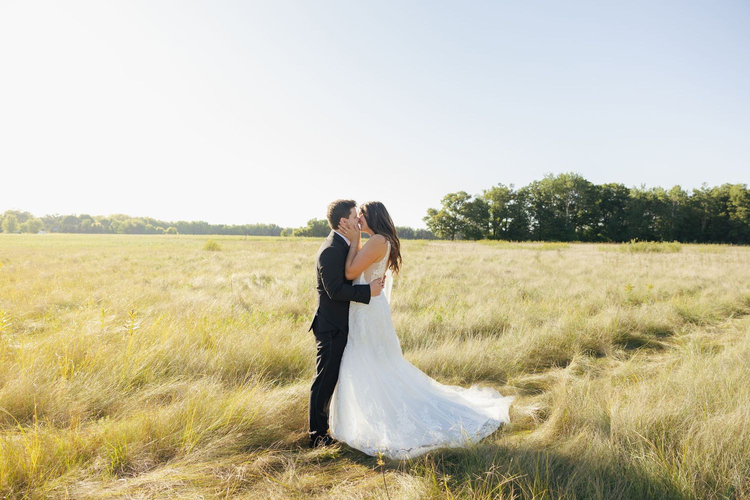 Bride and groom share a romantic kiss in a sunlit golden field on their wedding day.