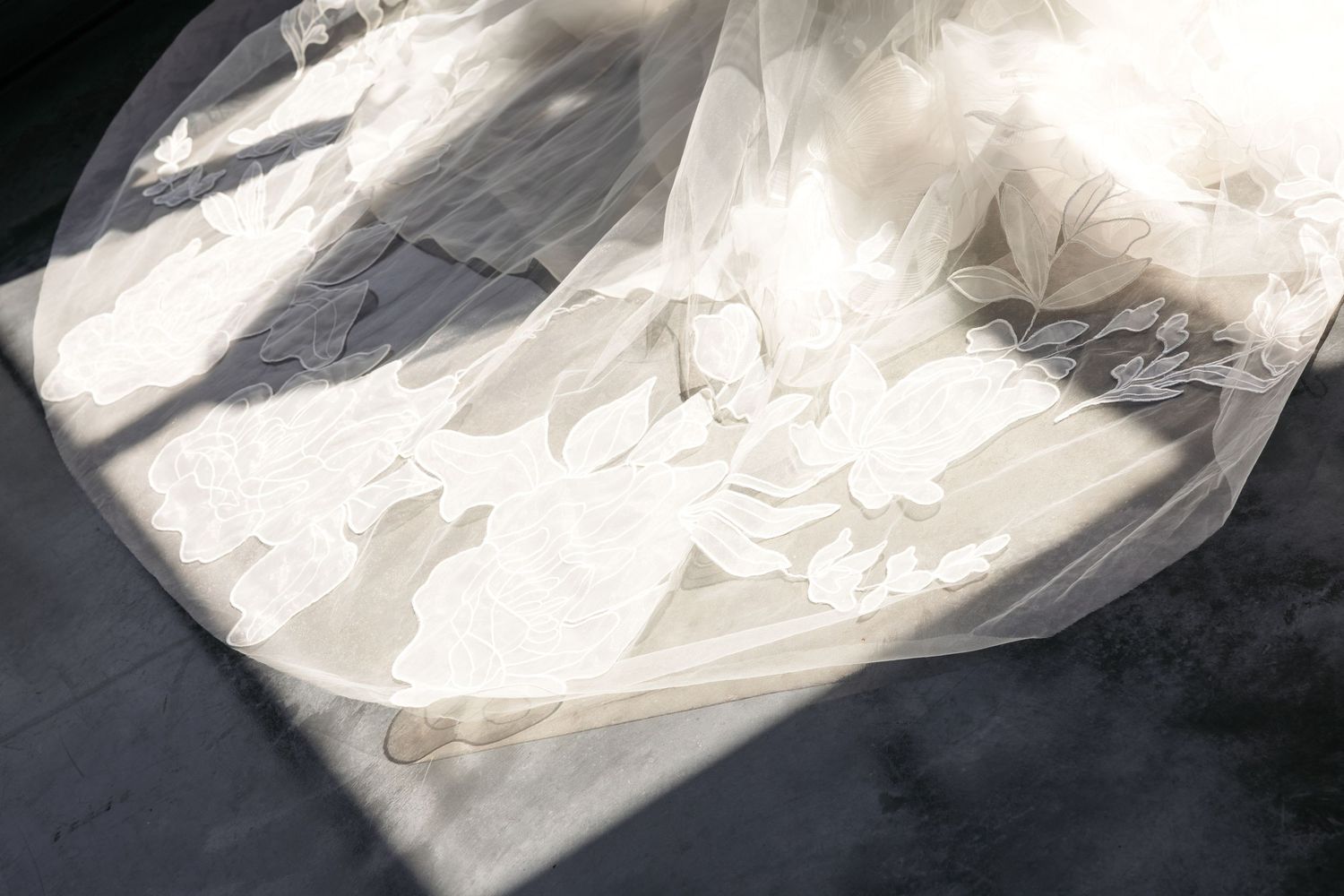 Elegant white bridal gown with delicate floral lace details laid flat, bathed in soft natural sunlight.