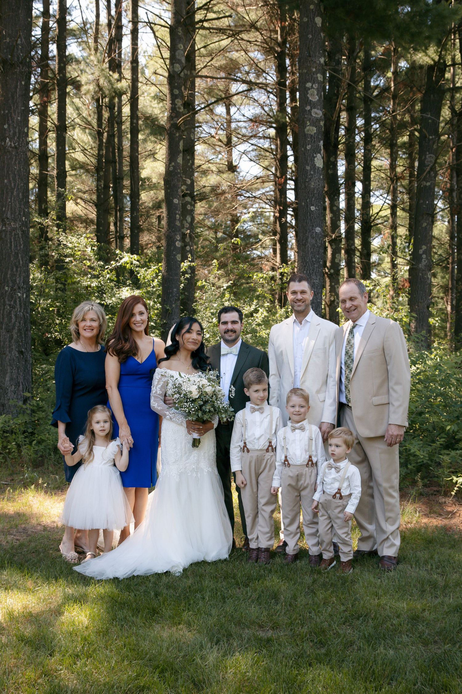 Wedding party and family group portrait standing in front of tall pine trees outdoors.