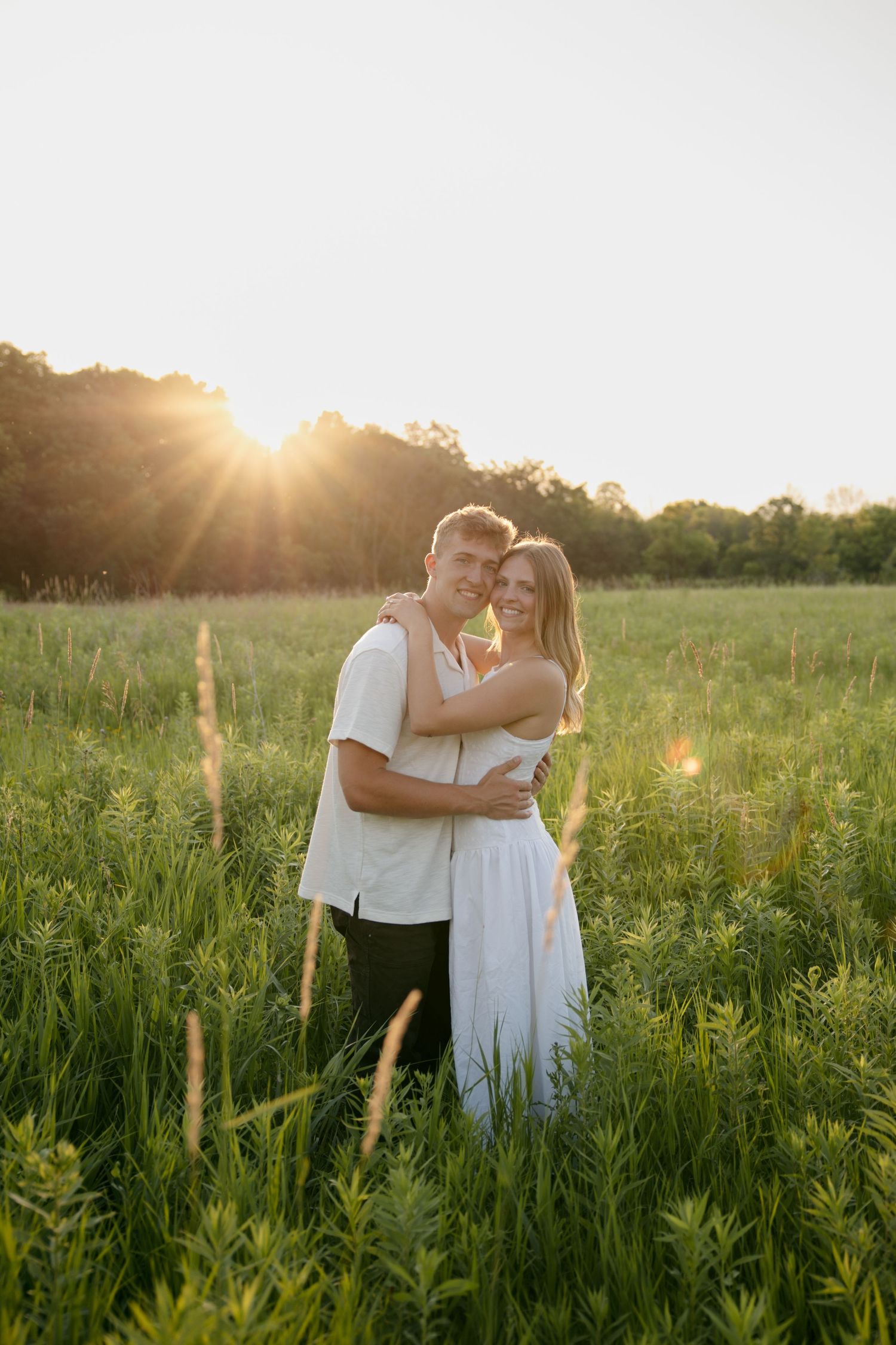 Happy couple embracing in a lush green meadow with a stunning sunburst in the background.
