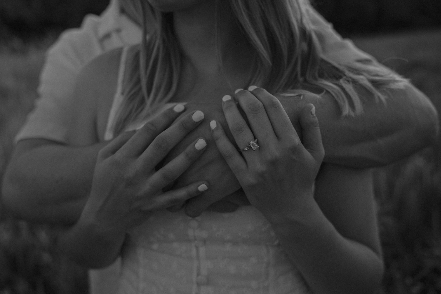 Close-up black and white photo of couple's hands, engagement ring visible on woman's finger.